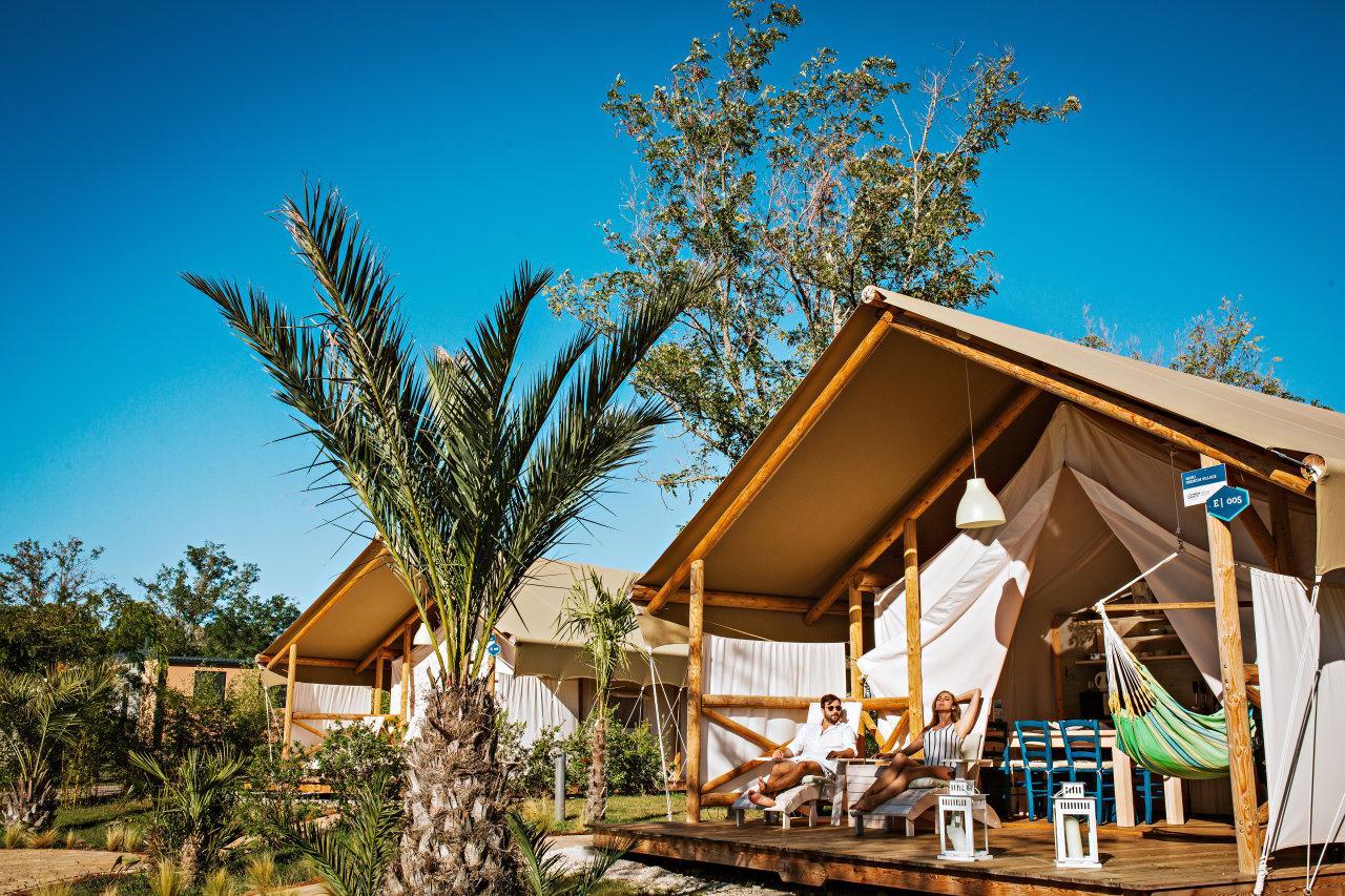 Ein Paar entspannt sich vor einem luxuri&ouml;sen Glamping-Zelt im Lanterna Premium Camping Resort