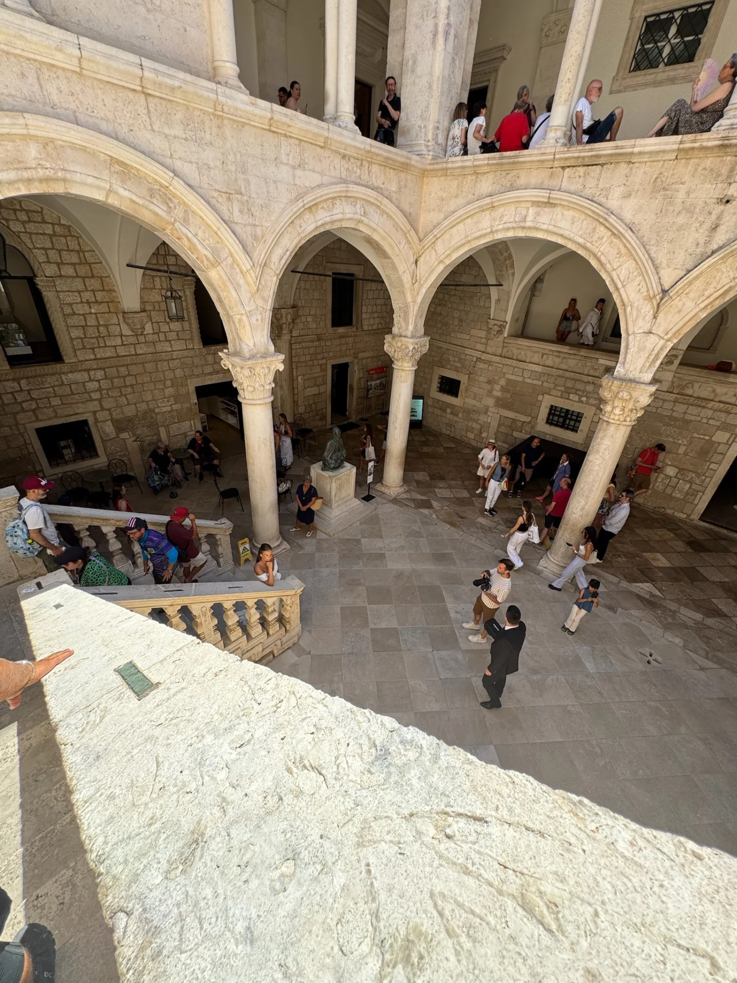 Historischer Innenhof des Rektorenpalasts in Dubrovnik mit Steinb&ouml;gen, S&auml;ulen und Besuchern.

