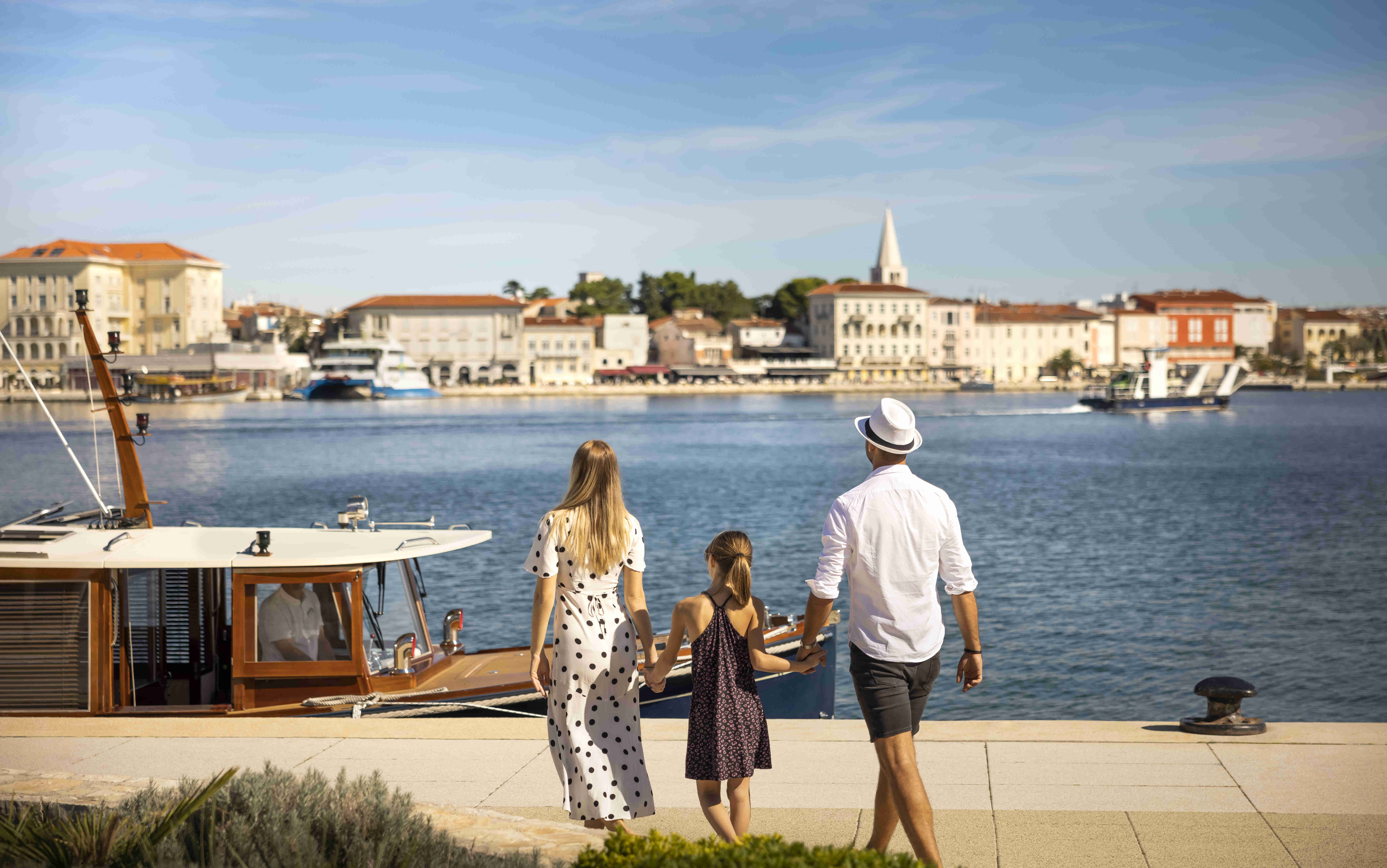 Eine Familie geht Hand in Hand an der Promenade mit der Altstadt Poreč im Hintergrund