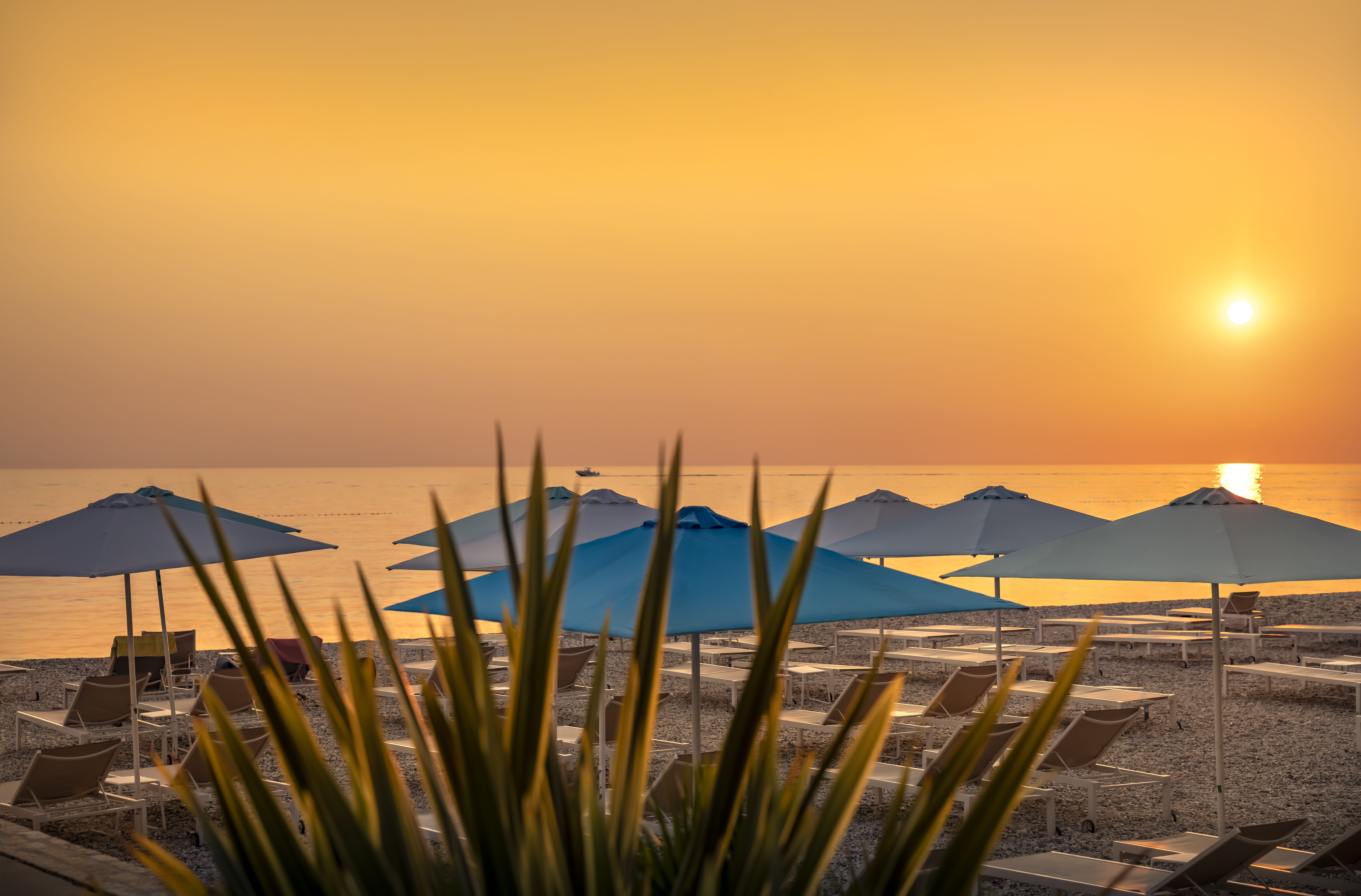 Blick auf den Sonnenuntergang vom Kiesstrand mit Sonnenschirmen
