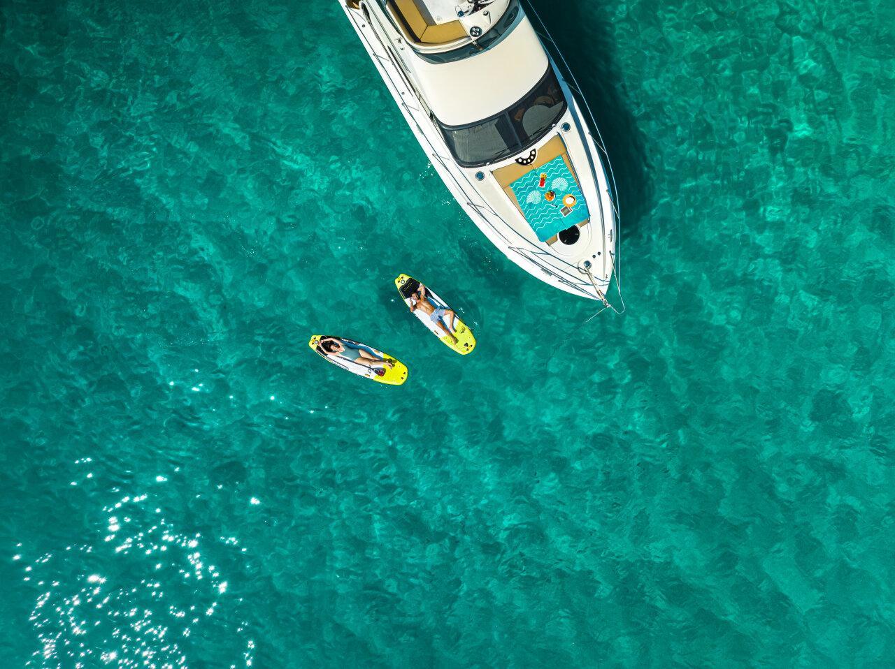 Paddleboarders enjoying the crystal-clear waters next to a private yacht Paddleboarder genießen das kristallklare Wasser neben einer Privatyacht