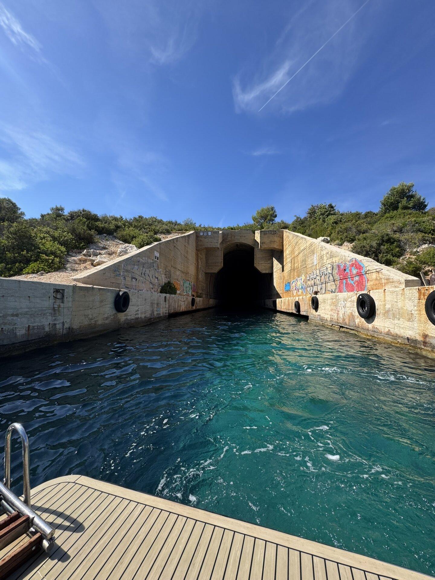Pogled iz broda pri ulasku u vojni podmorski tunel iz doba Jugoslavije na otoku Visu, s grafitima na zidovima i tirkiznom vodom