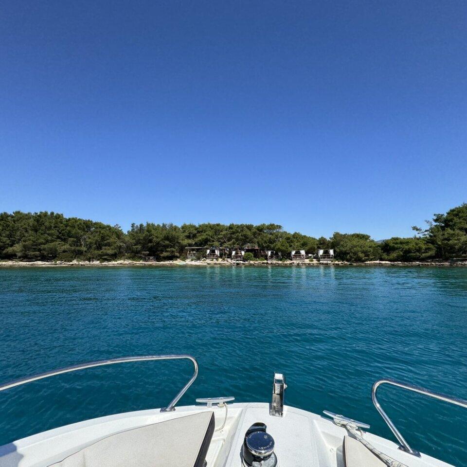 Ein Blick vom Boot zeigt eine abgelegene mit Pinien bewachsene Insel mit rustikalen Cabanas, umspült von einladendem, türkisfarbenem Wasser