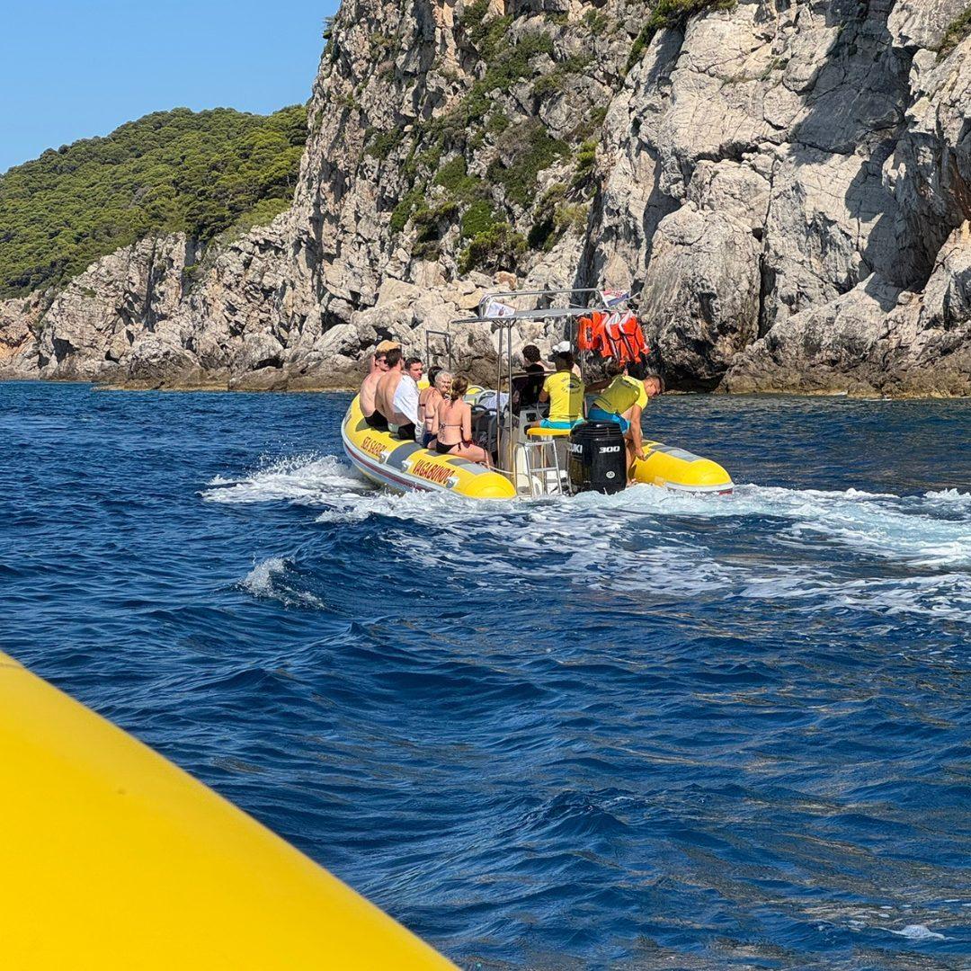 Sea safari boat with passengers cruising away from rocky cliffs, heading toward Lopud Island