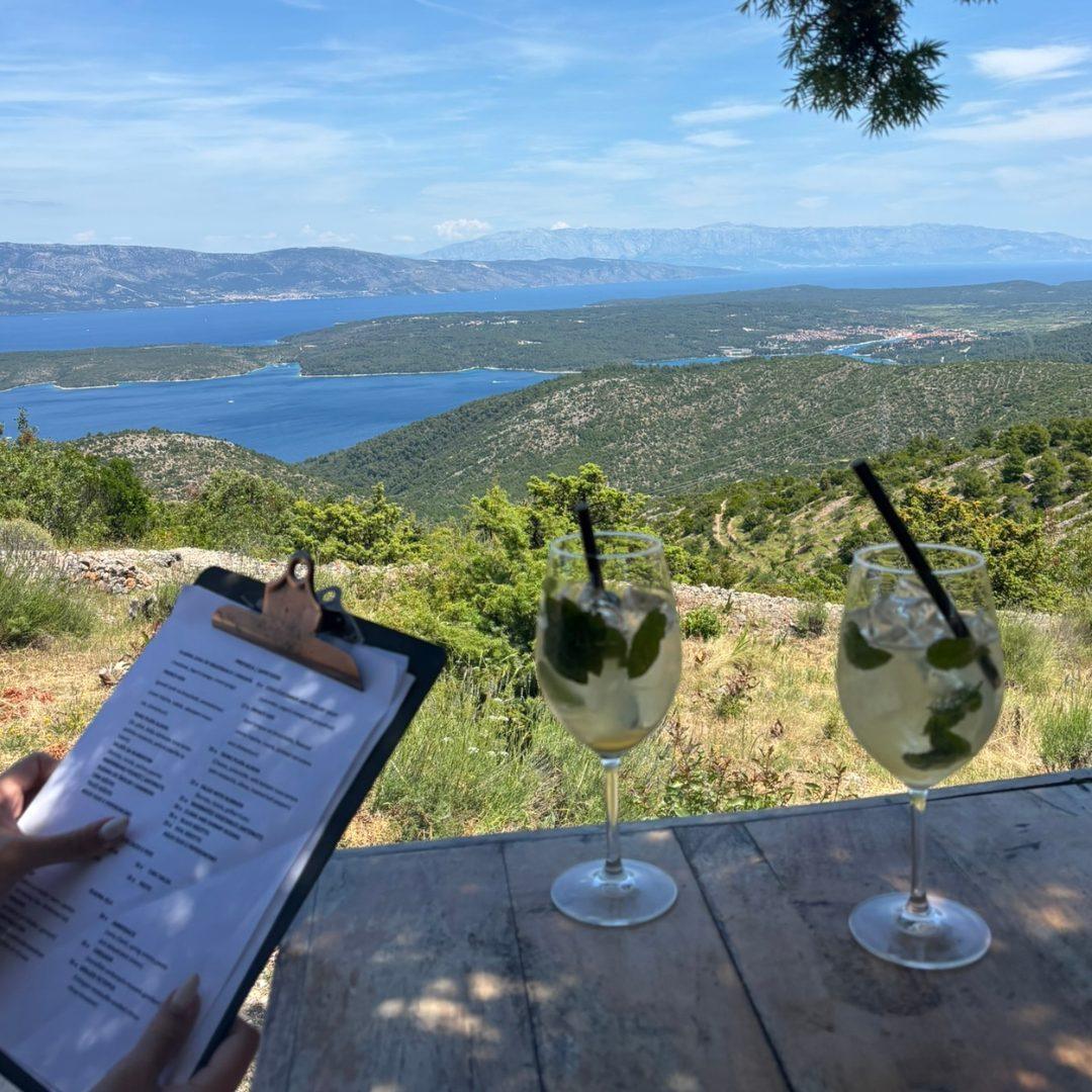 Two glasses of non-alcoholic cocktails with mint, set on a rustic table overlooking the hills, islands, and blue waters of the Adriatic from Alavia Soulfood.