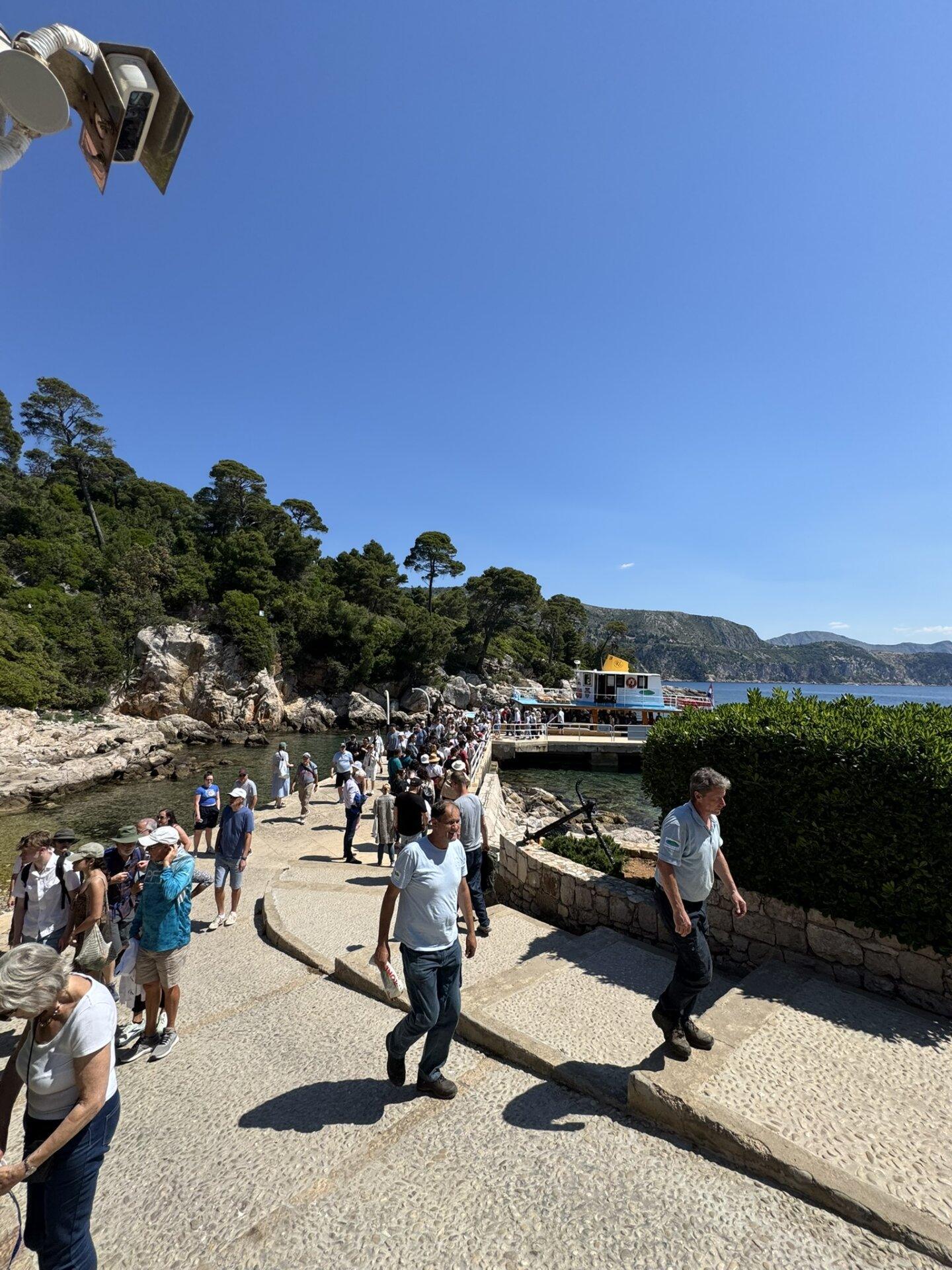 Visitors disembarking from the ferry at Lokrum Island’s main pier, surrounded by rocky shoreline, pine trees, and clear blue skies.