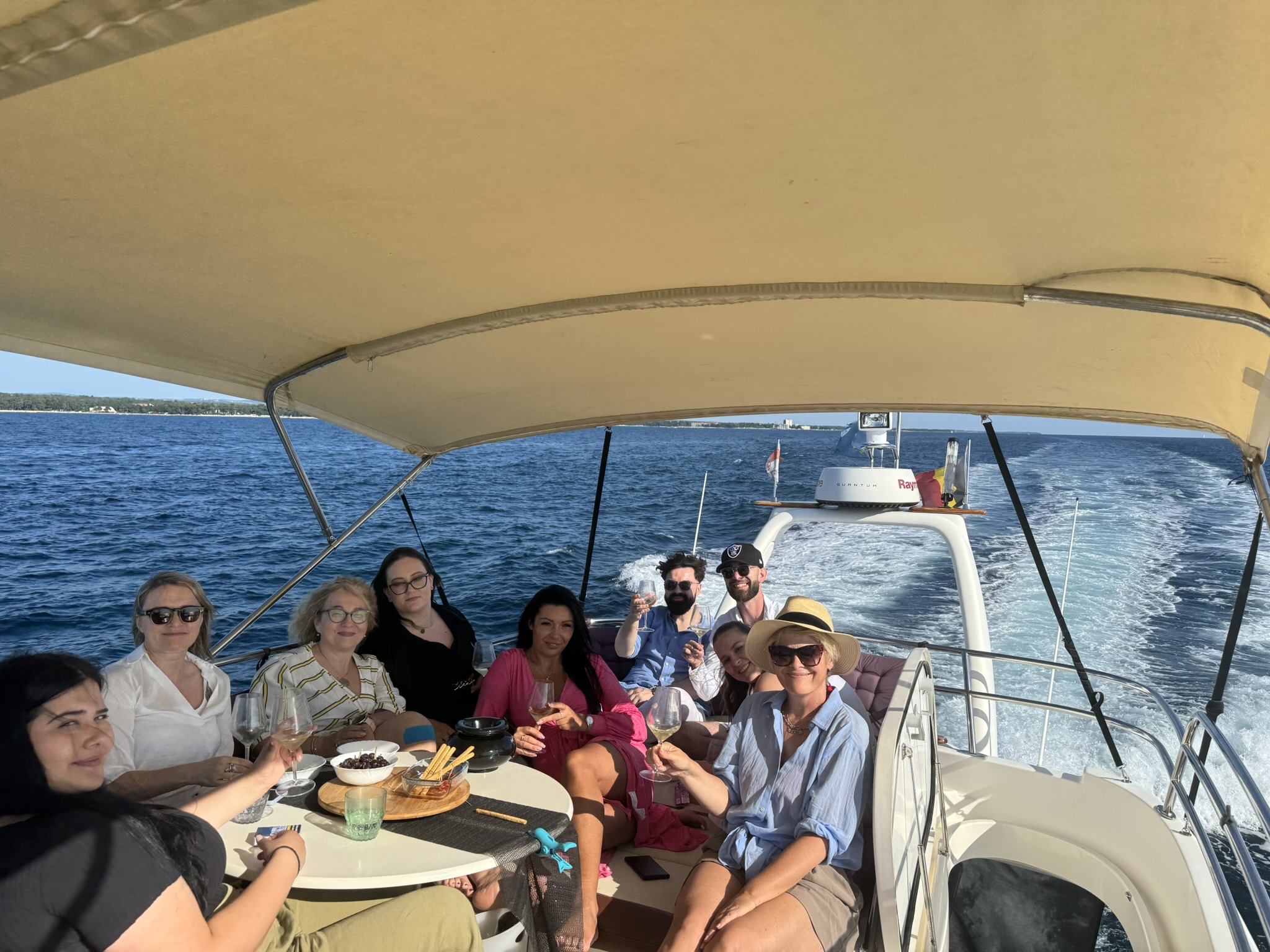 Group of friends relaxing with wine on the fly-bridge of a moving yacht, trailing wake behind.