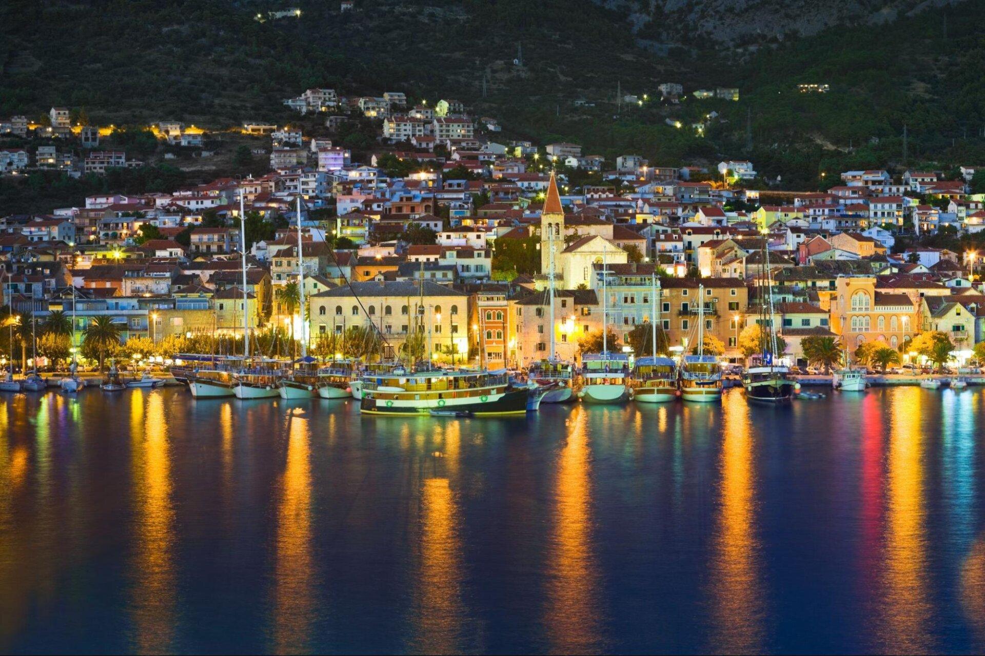 Nachtpanorama von Makarska mit beleuchteter K&uuml;stenpromenade und verankerten Booten