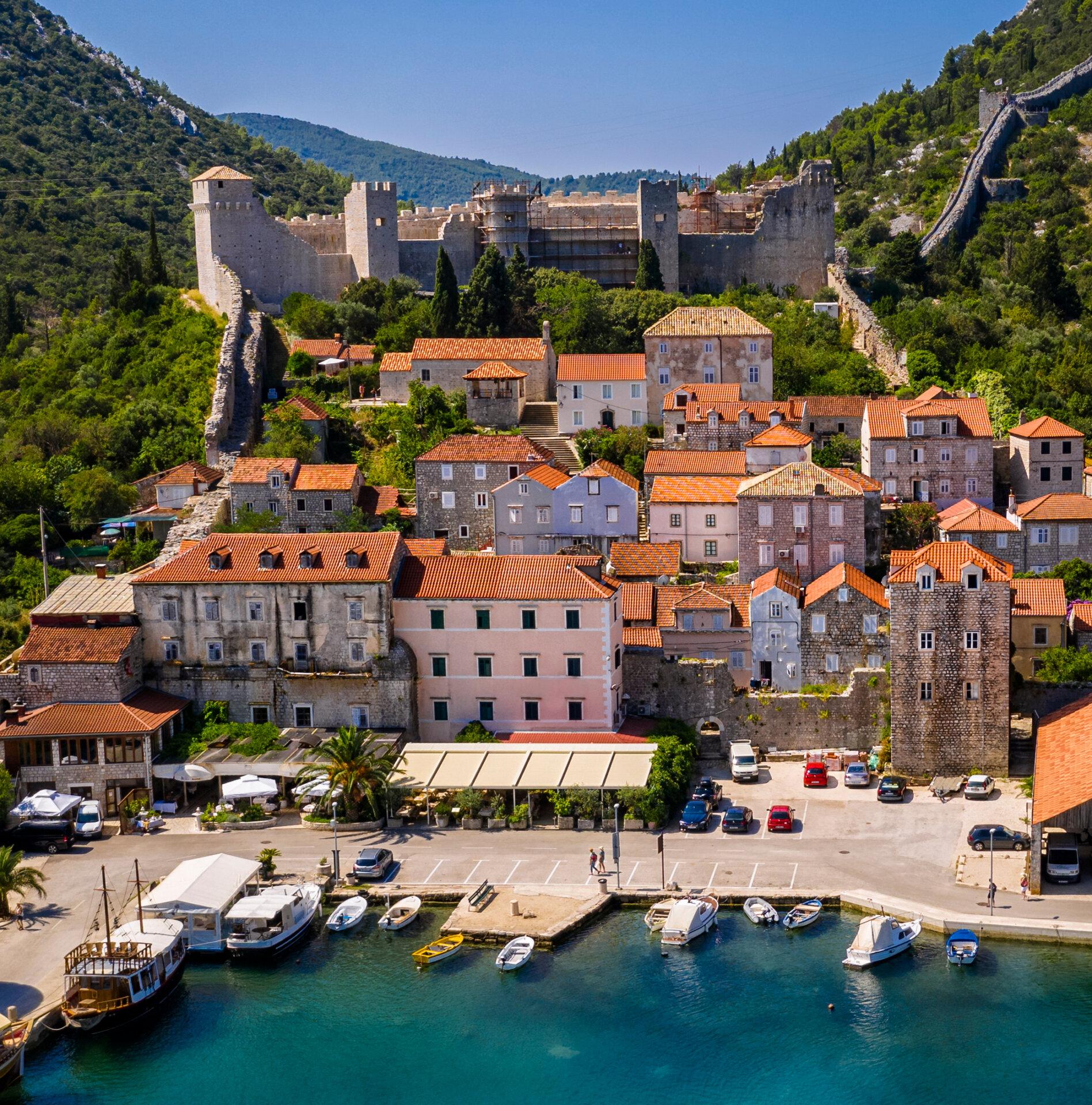 Luftansicht der historischen Stadt Ston, Kroatien, mit steinernen Wehrmauern aus dem Mittelalter, Häusern mit Terracotta-Dächern und einem Hafengebiet mit aneinandergereihten Booten