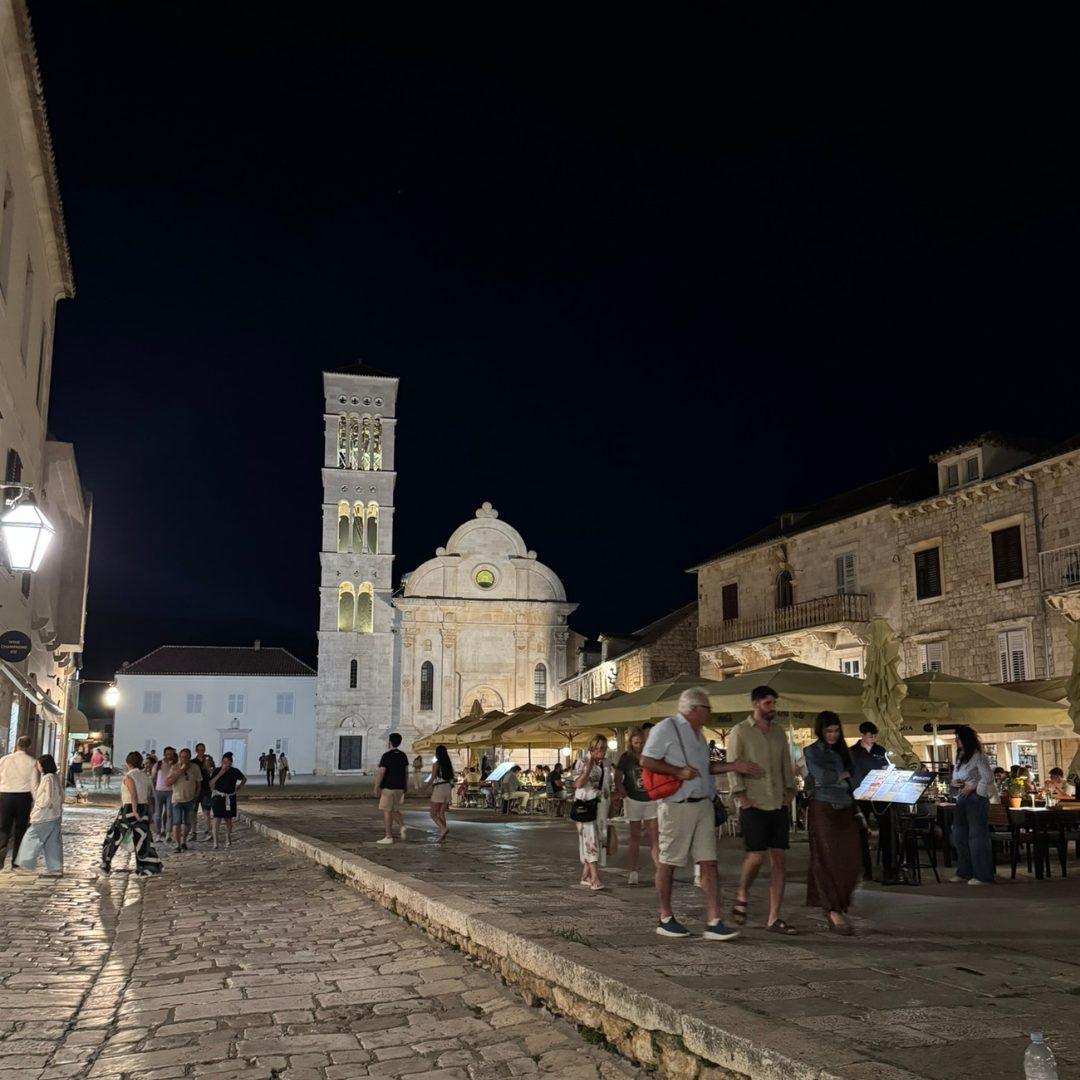 St. Stephen’s Cathedral illuminated at night in Hvar Town, with people walking across the stone-paved main square.