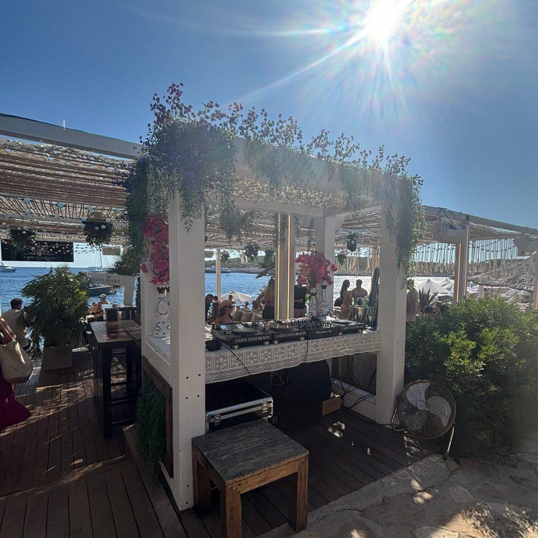 Outdoor bar at Carpe Diem Beach on Stipanska Island, decorated with flowers and overlooking the Adriatic Sea under the afternoon sun.