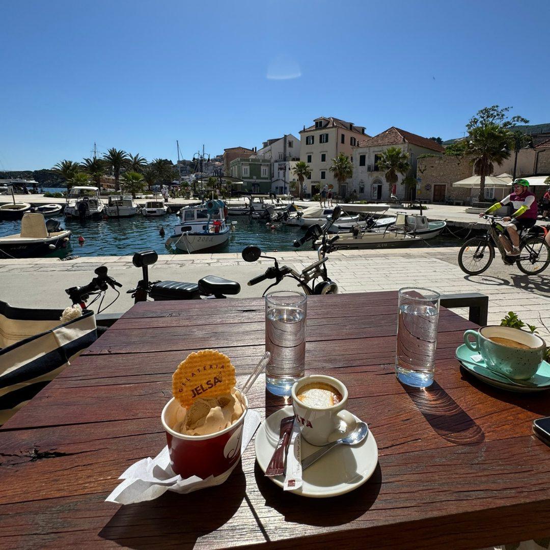 Coffee and gelato are served at a waterfront café in Jelsa, with boats docked in the harbour and colourful houses in the background.