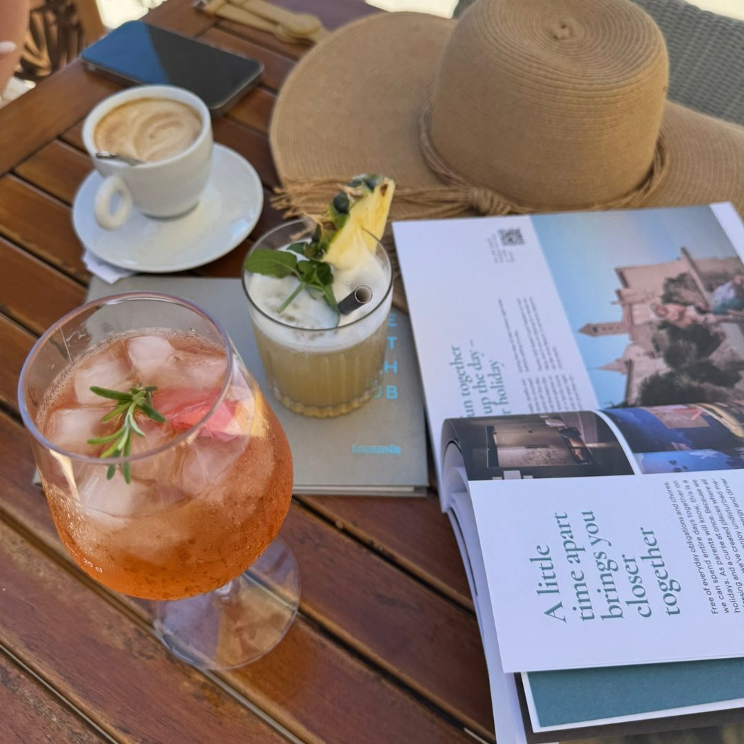 Table with a coffee, cocktails, a hat, a magazine and a phone.