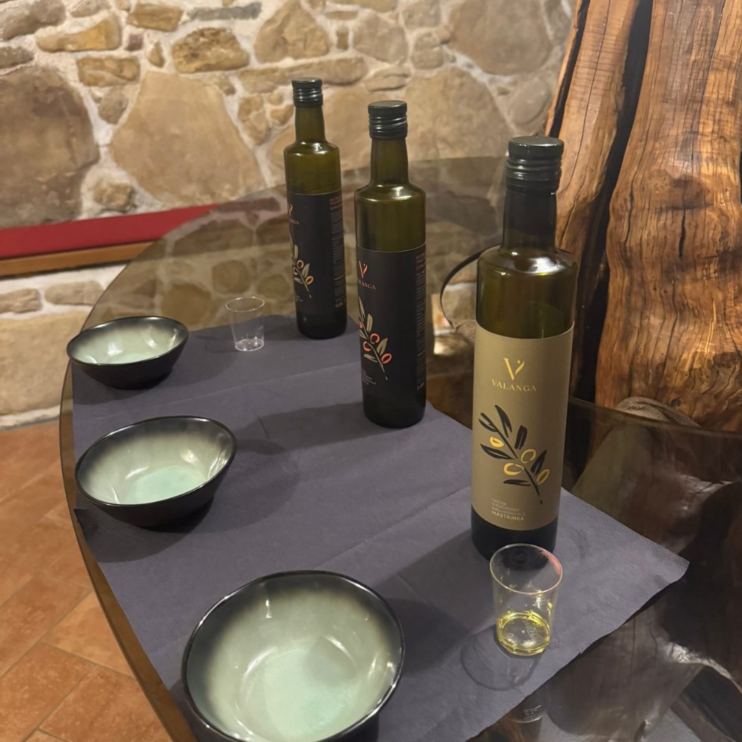 Bottles of Valanga olive oil with tasting bowls and glasses set on a rustic wooden table.