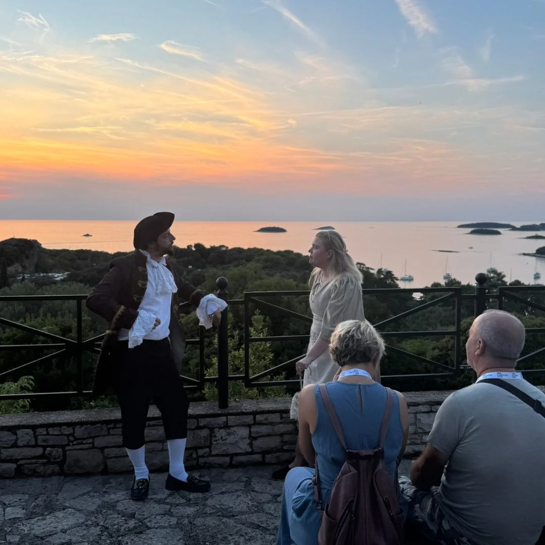 Casanova und eine weibliche Figur bei Sonnenuntergang an einem Aussichtspunkt in Vrsar spielen eine Szene vor dem Publikum. 