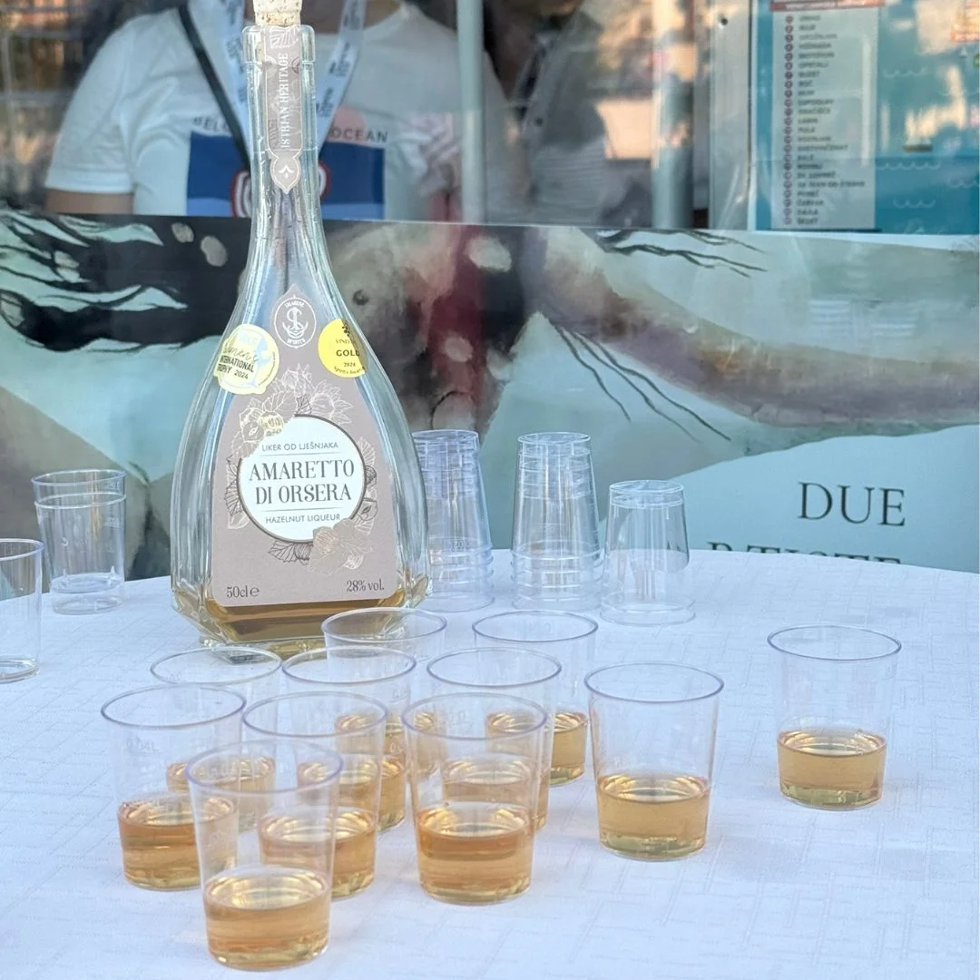 Flasche und Verkostungsgl&auml;ser mit Haselnusslik&ouml;r Amaretto di Orsera, ausgestellt vor dem Tourismusb&uuml;ro