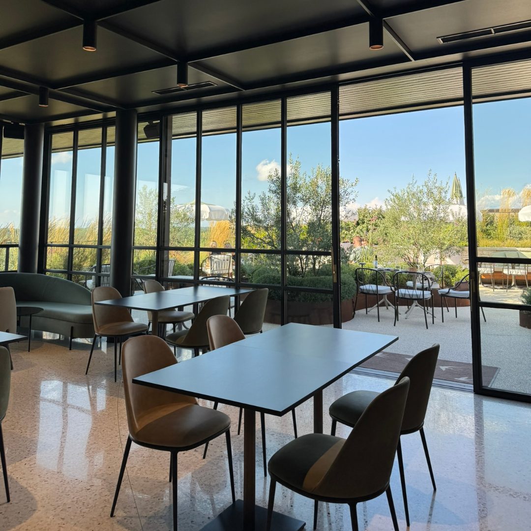 Modern indoor seating area at Radovan Wines with large glass windows opening to a terrace surrounded by greenery and umbrellas.
