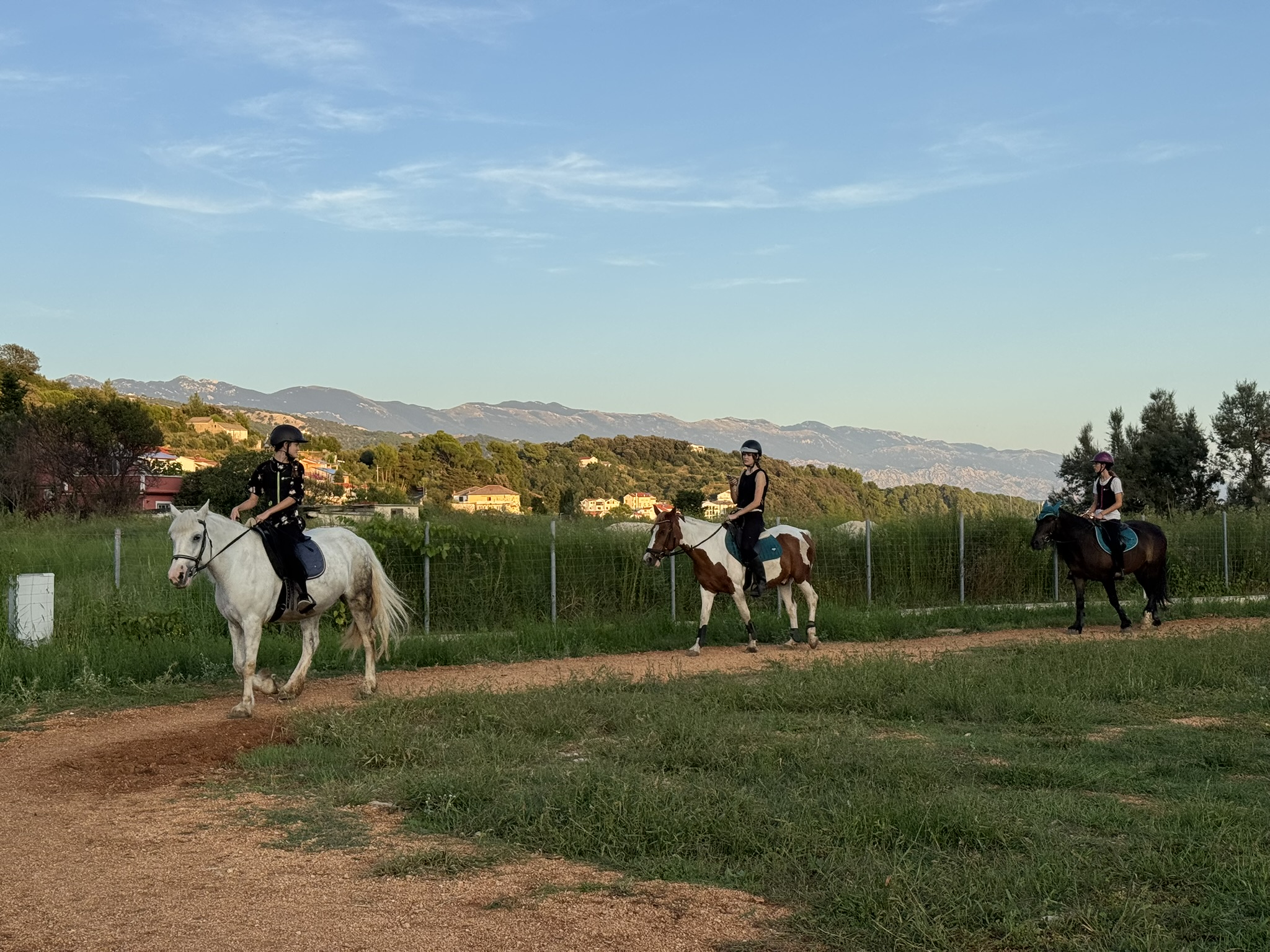 Group of riders on horseback at Soline Ranch, Rab Island, with rolling hills and mountains in the background at sunset.