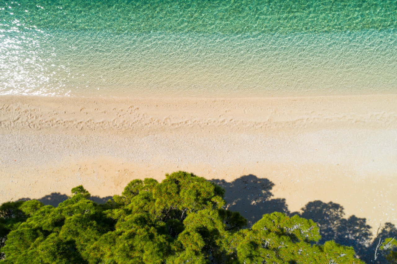 Aerial view of a sandy-pebble beach with turquoise sea and pine trees near Hotel Meteor in Makarska.