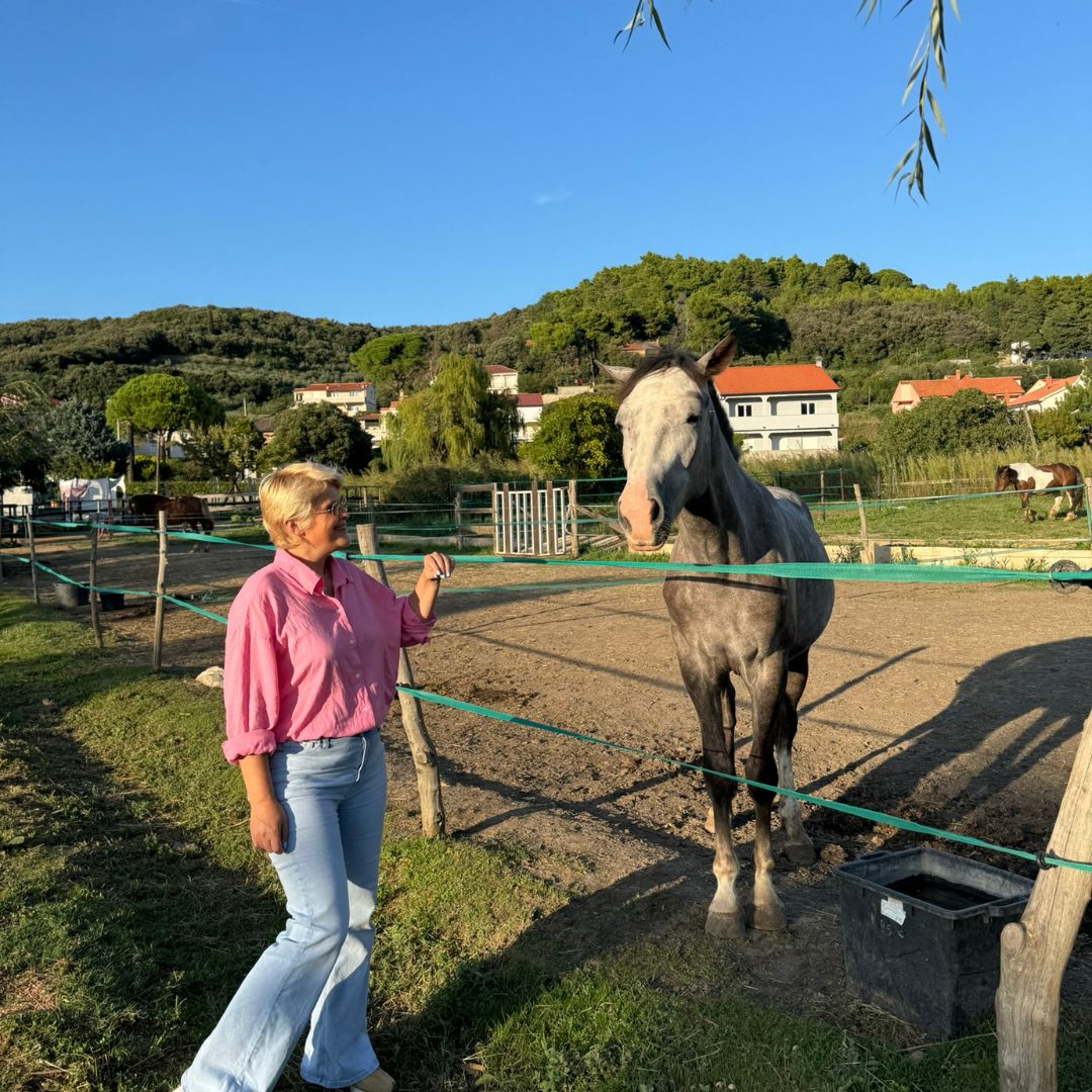 Woman standing beside a horse at Soline Ranch on Rab Island, surrounded by greenery and stables.