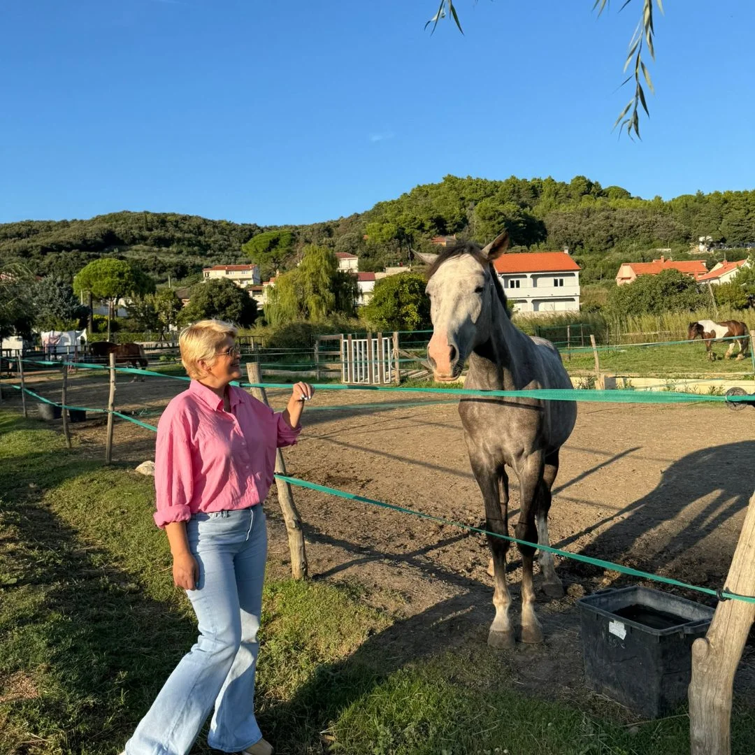 Eine Frau steht neben einem Pferd auf der Soline-Ranch auf der Insel Rab, umgeben von Gr&uuml;n und St&auml;llen. 