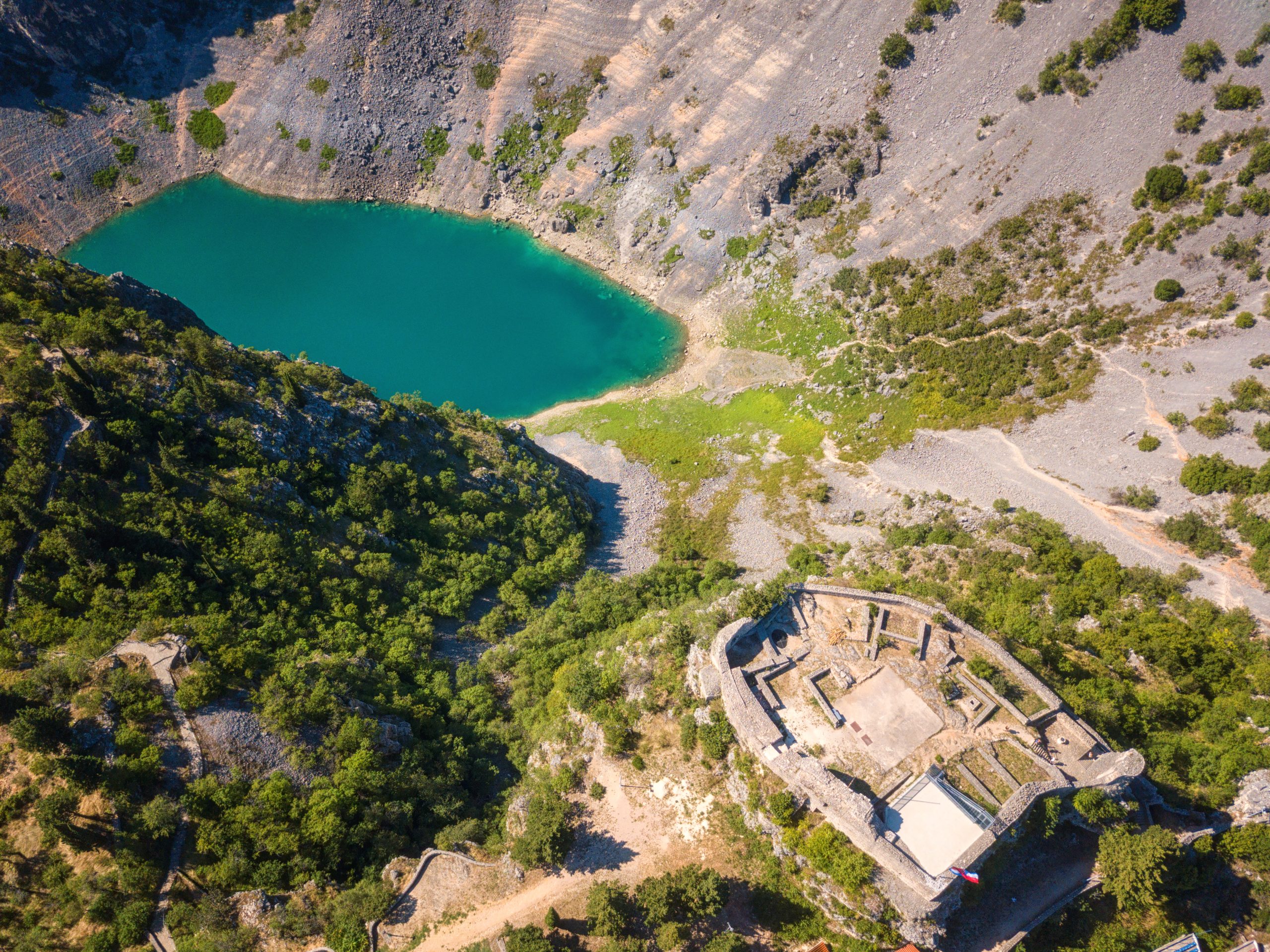 Aerial view of the Blue Lake (Modro jezero) in Imotski with turquoise water and nearby fortress ruins.