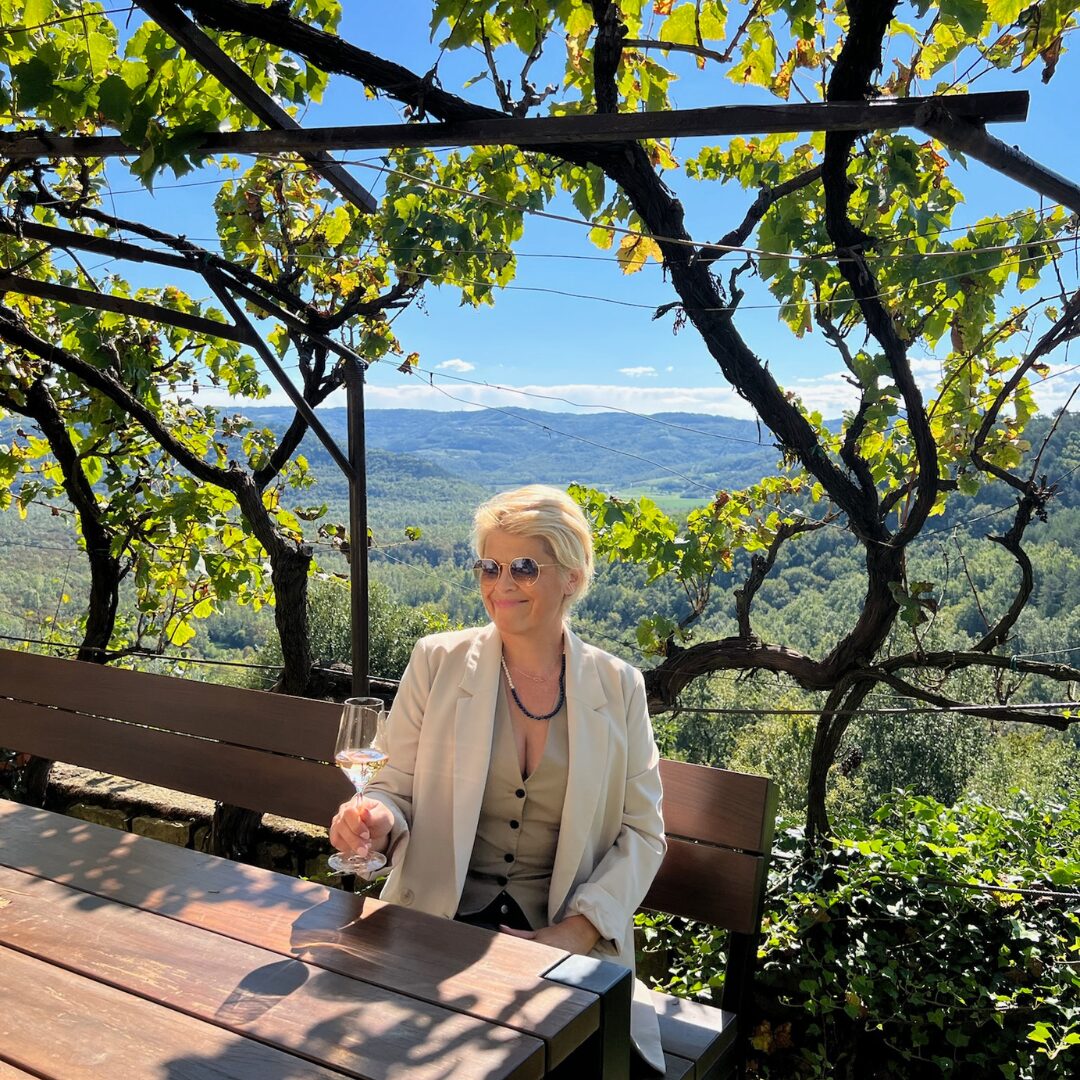 Guest enjoying a glass of wine on a vine-covered terrace overlooking Istria’s green hills.
