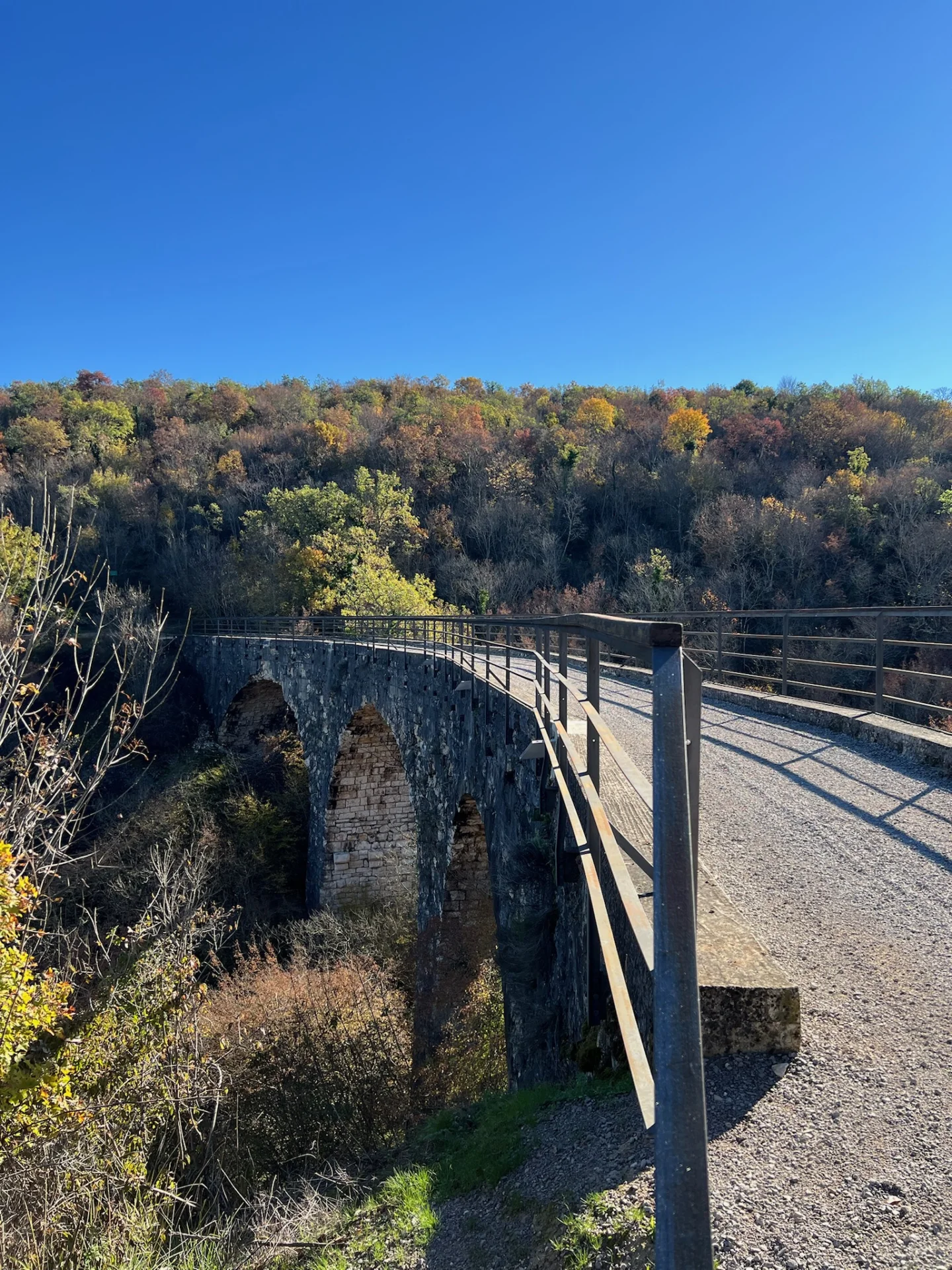 Der Viadukt von Sabadine auf dem Parenzana-Weg: Steinb&ouml;gen mit Schotterbelag und Gel&auml;ndern &uuml;ber einer bewaldeten Schlucht im Herbstlicht. 