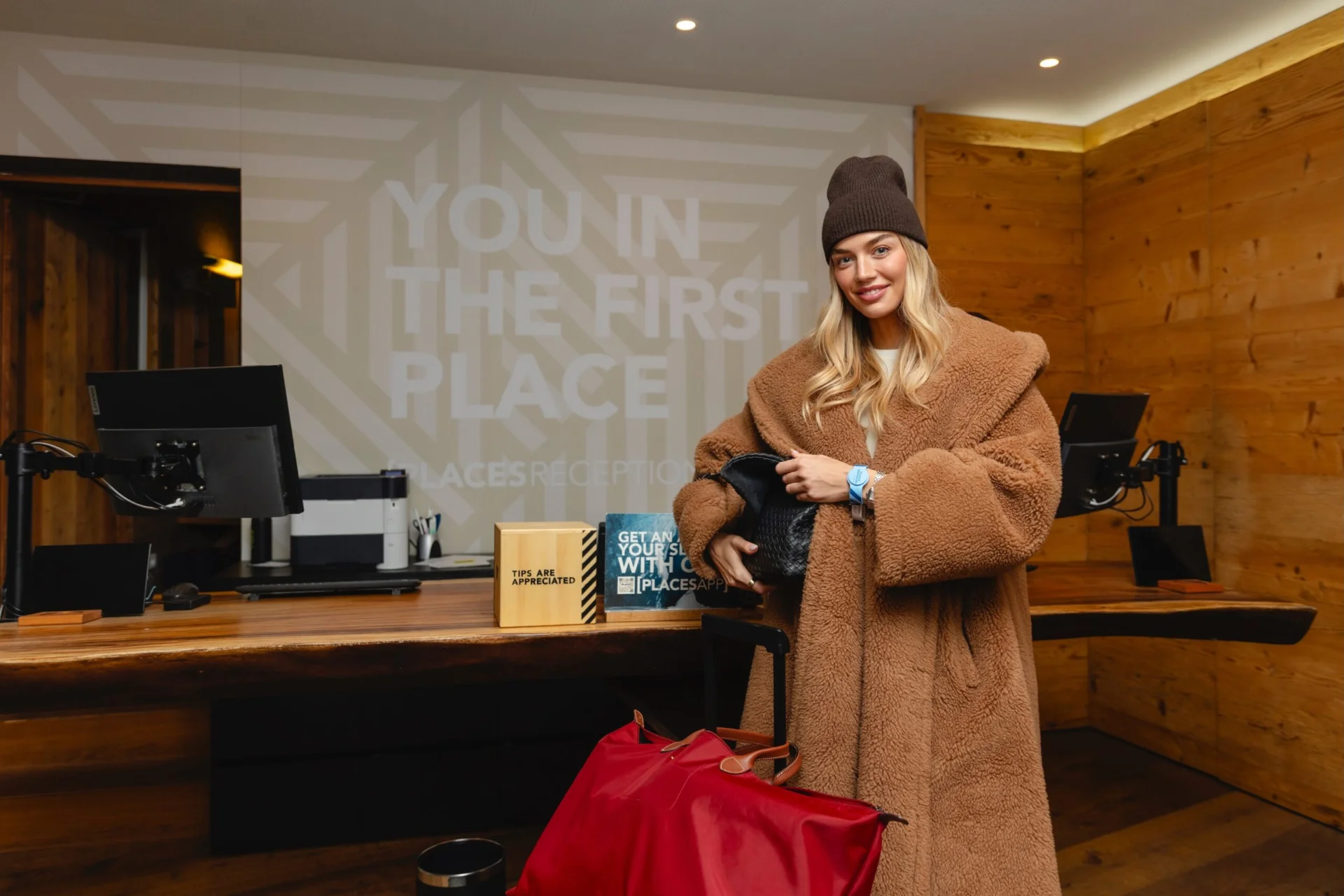 Ein Gast checkt im Winteroutfit und mit Gepäck an der Rezeption des PLACES Obertauern by Valamar ein.