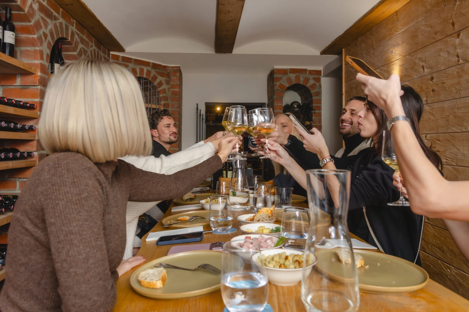 Eine Gruppe von Gästen stößt bei einer Weinverkostung und einem gemeinsamen Abendessen in einem alpinen Speisesaal in Obertauern an.