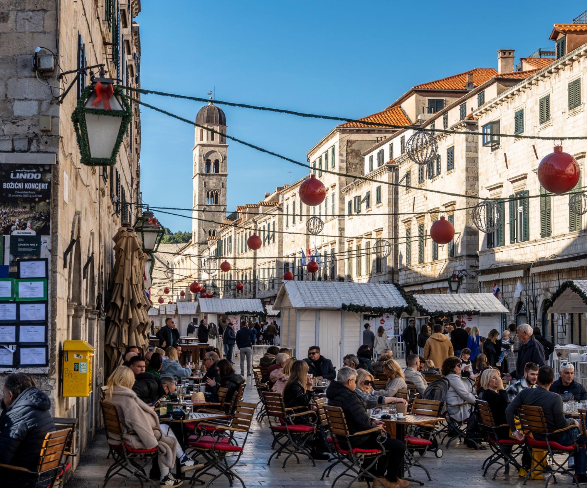 People enjoying outdoor cafés and festive stalls on a decorated street in Dubrovnik during Advent.