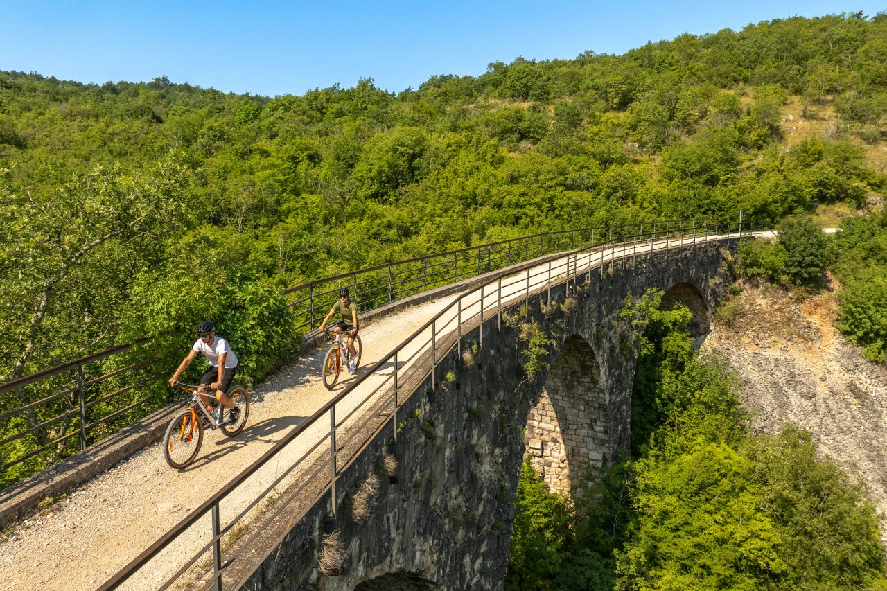 Radfahrer fahren auf dem Parenzana-Radweg über ein Steinviadukt, umgeben von den grünen Hügeln Istriens. Radfahrer fahren auf dem Parenzana-Radweg über ein Steinviadukt, umgeben von den grünen Hügeln Istriens.