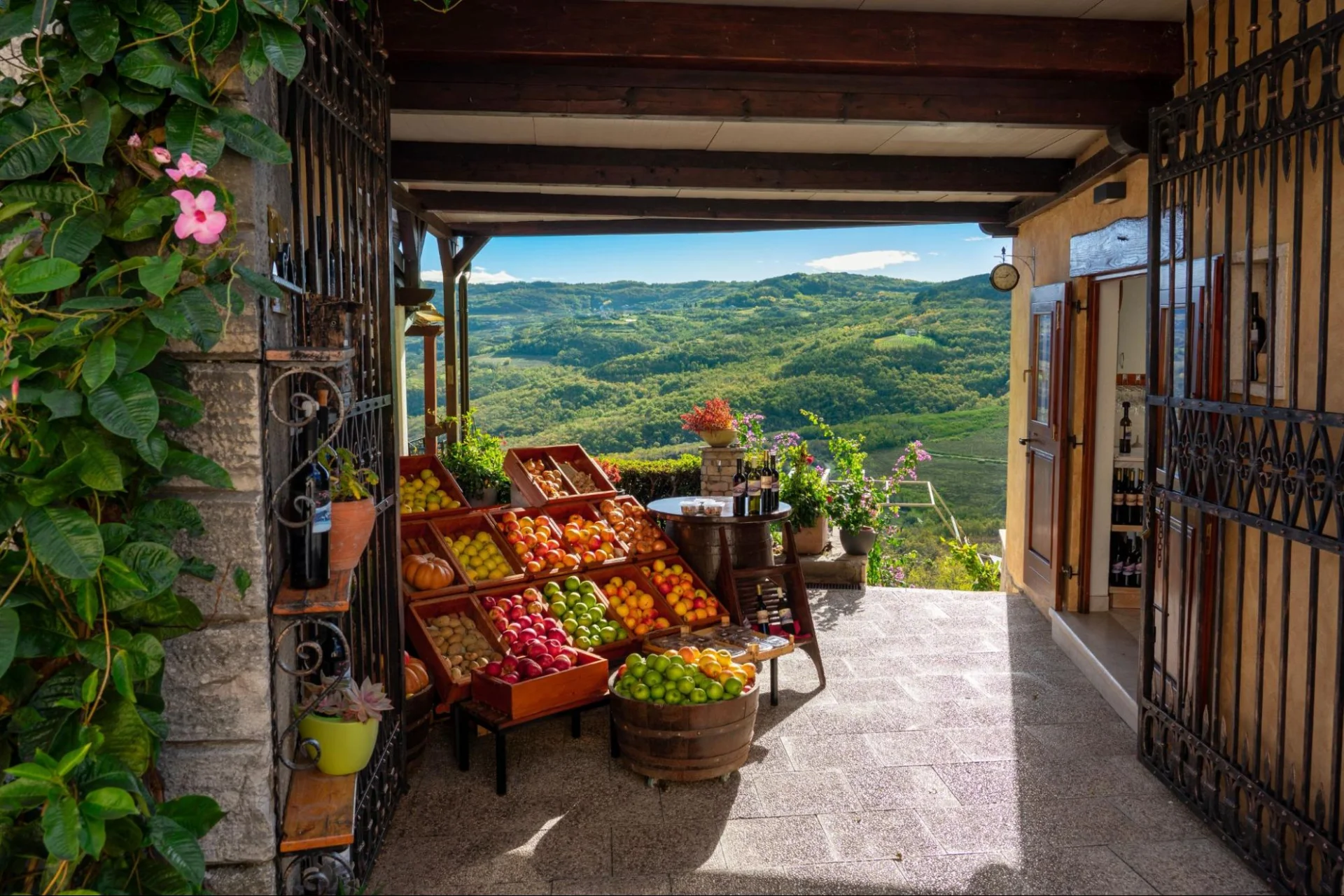 Rustikale Terrasse mit K&ouml;rben voller frischem Obst und Blick auf gr&uuml;ne H&uuml;gel und Weinberge. 