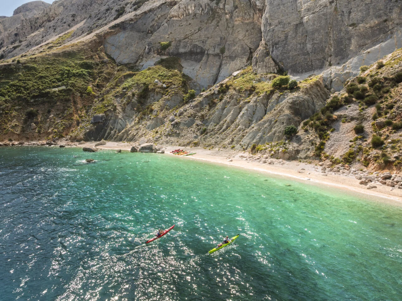 Zwei Personen, die im klaren, t&uuml;rkisfarbenen Meer der Adria in der N&auml;he eines abgelegenen Strandes und felsiger Klippen auf der Insel Rab Kajak fahren. 