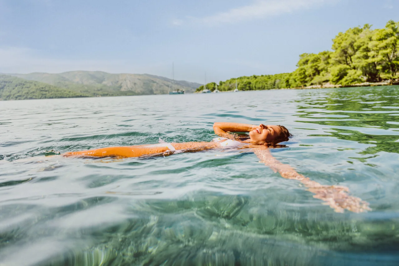 Eine Frau schwimmt friedlich im klaren Meer der Adria in der N&auml;he einer gr&uuml;nen Inselk&uuml;ste an einem sonnigen Tag. 
