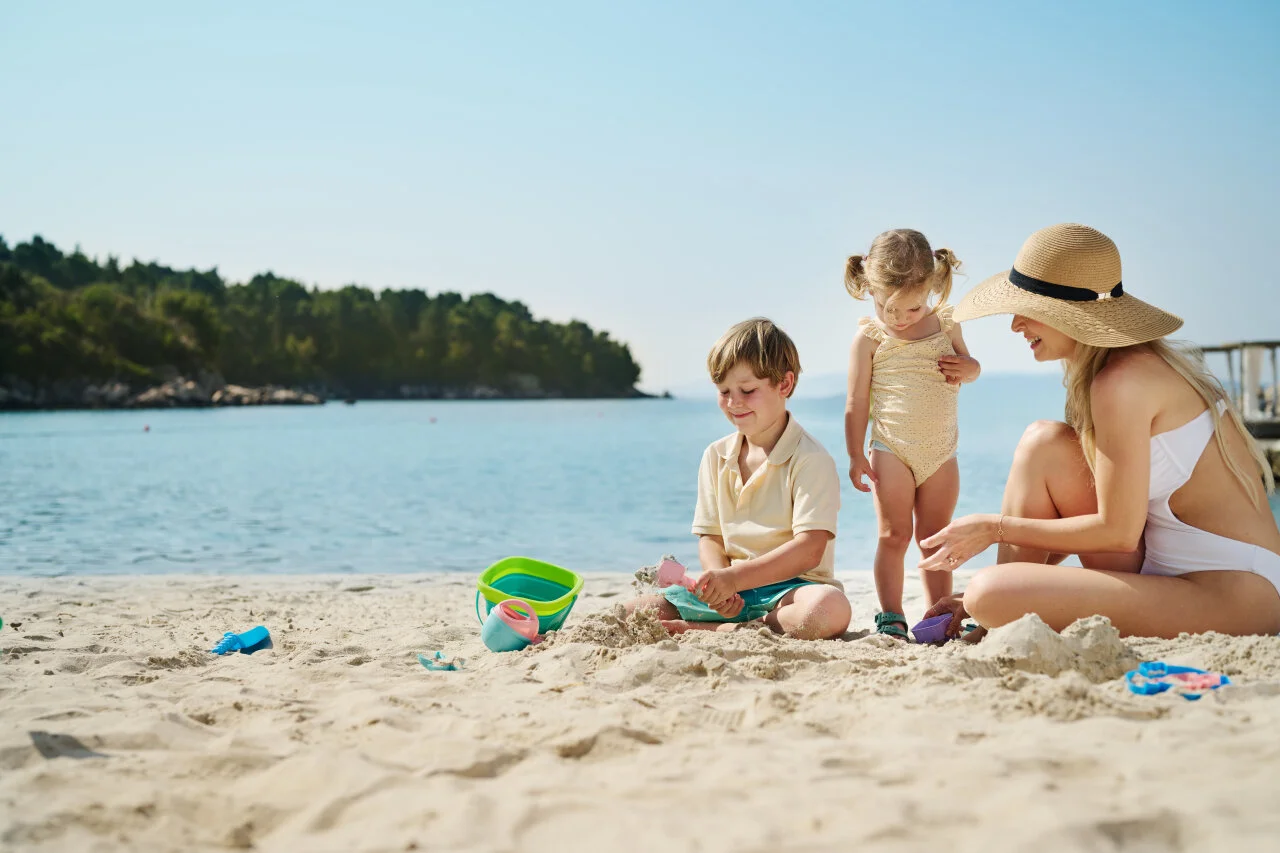 Mutter und zwei kleine Kinder spielen im Sand an einem sonnigen Strand am Adriatischen Meer.