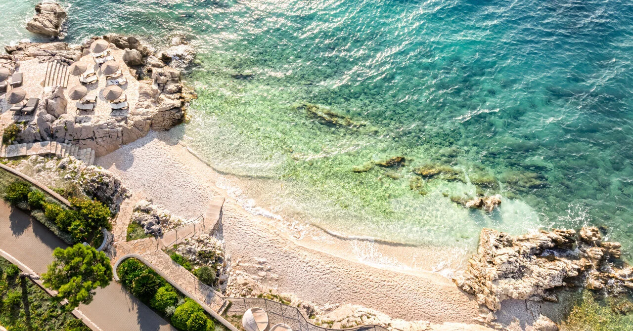 Luftaufnahme eines Sandstrandes mit der türkisfarbenen Adria, steinernen Sonnenterrassen und Küstenpfaden in Rabac.
