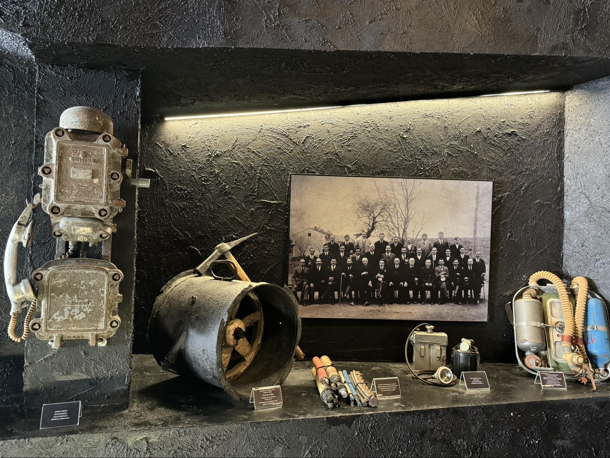 Historic mining equipment, tools, and an old group photograph displayed in an underground mining museum exhibition.