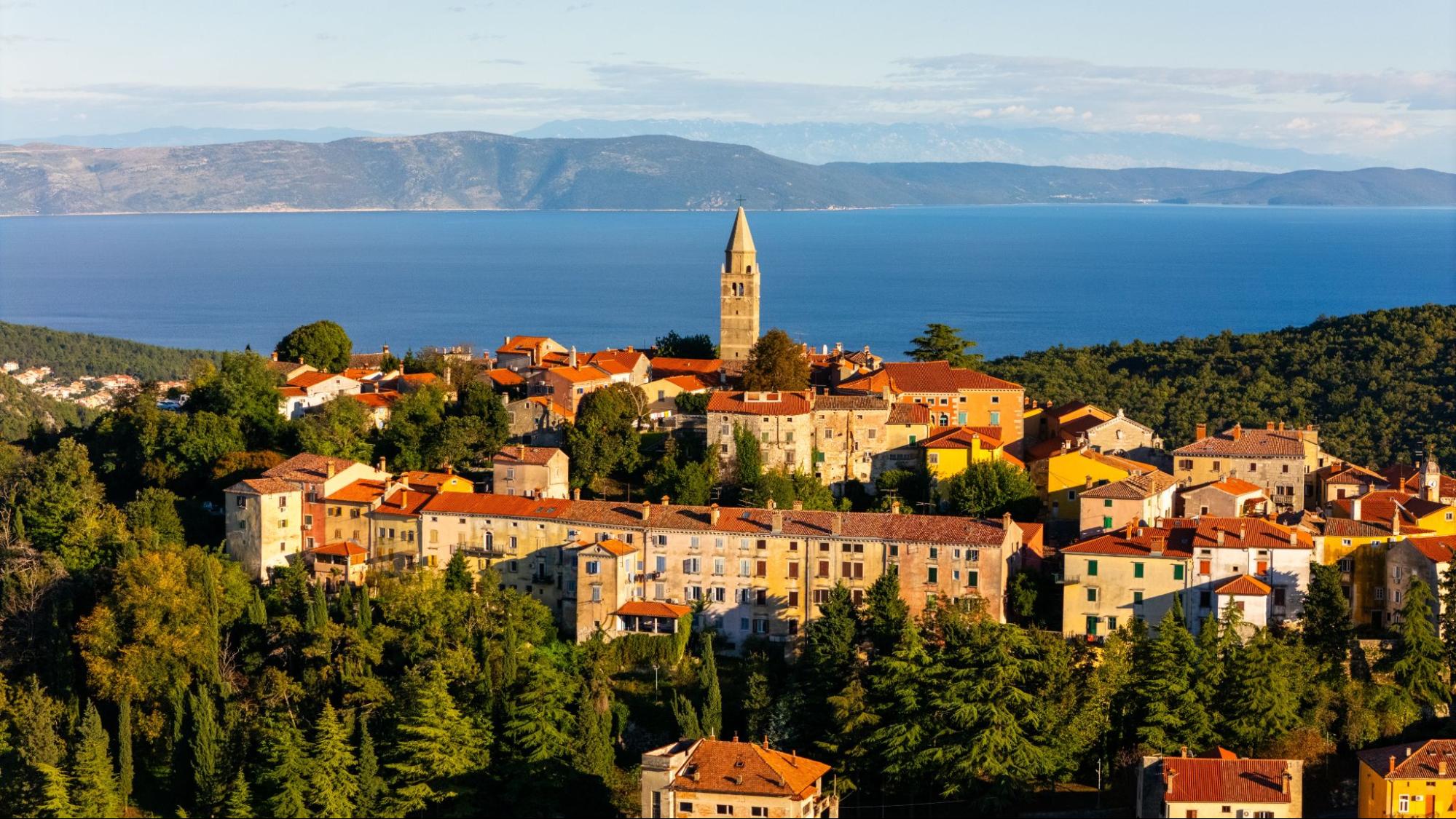 Panoramic view of Labin Old Town with terracotta rooftops overlooking the Adriatic Sea and distant mountains.