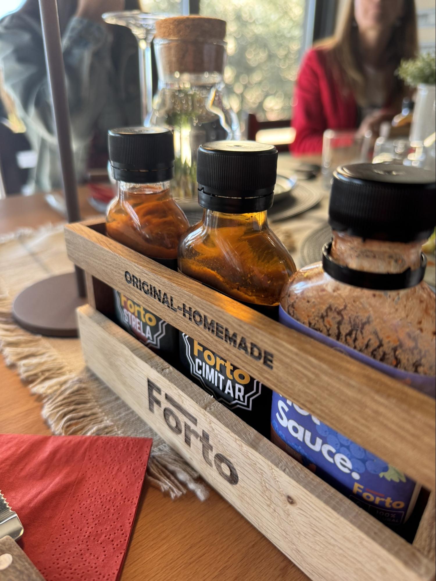 Selection of homemade hot sauces in glass bottles displayed in a wooden holder on a restaurant table.