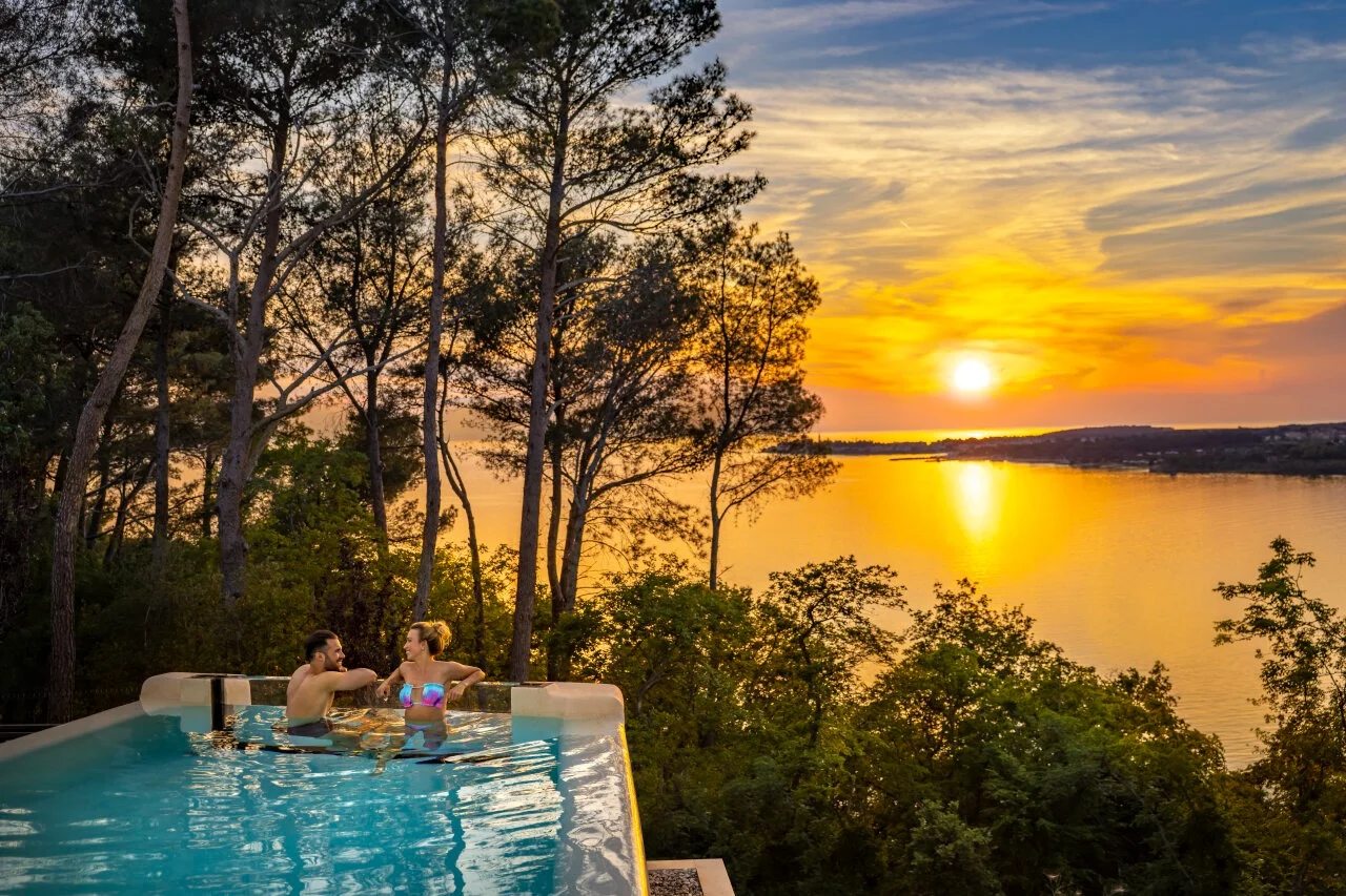 Ein Paar im Infinity-Pool des Punto Blu Valamar Camping Village genießt den Sonnenuntergang über dem Meer in Istrien