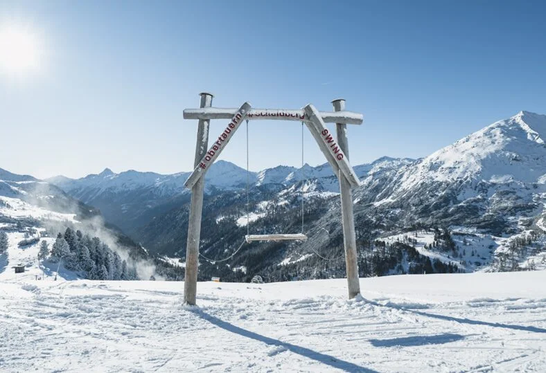 A panoramic swing at the top station of the Schaidbergbahn, overlooking snow-covered slopes with breathtaking mountain views.

