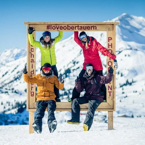 Four people posing for a photo inside the large #loveobertauern frame on the ski slope.