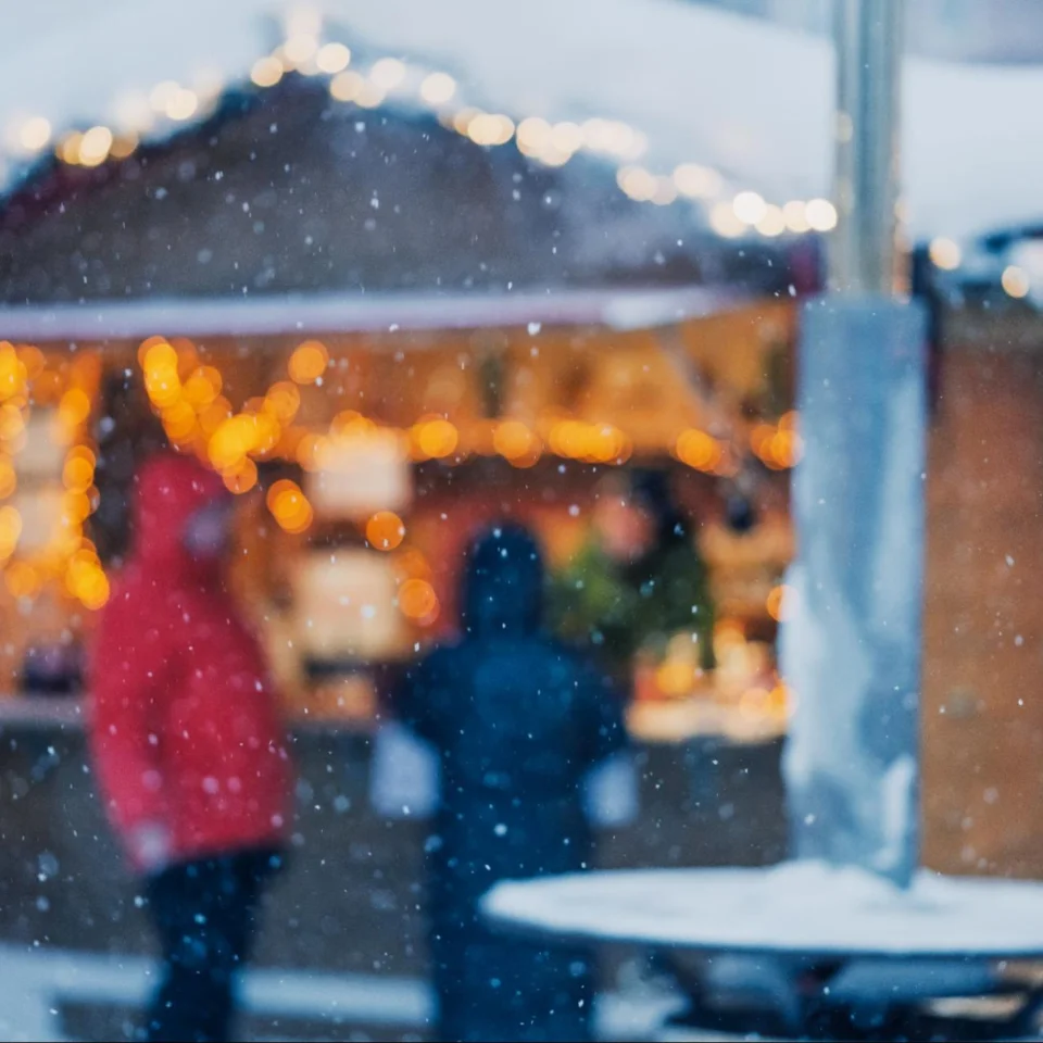 Visitors at a festive wooden hut in Obertauern with Christmas lights glowing through falling snow.