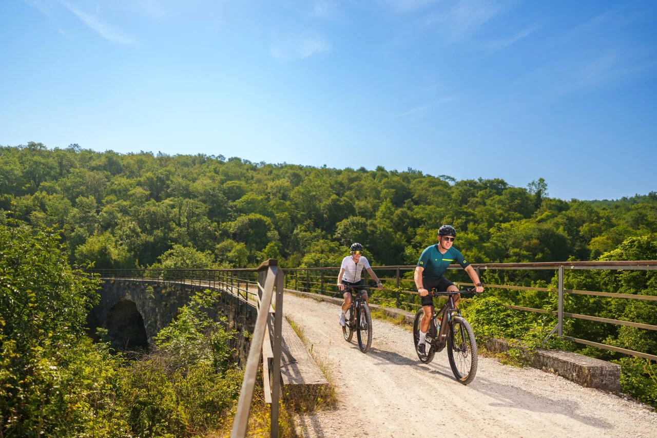 A couple cycling on a viaduct along the Parenzana trail in Istria on a sunny spring day.
