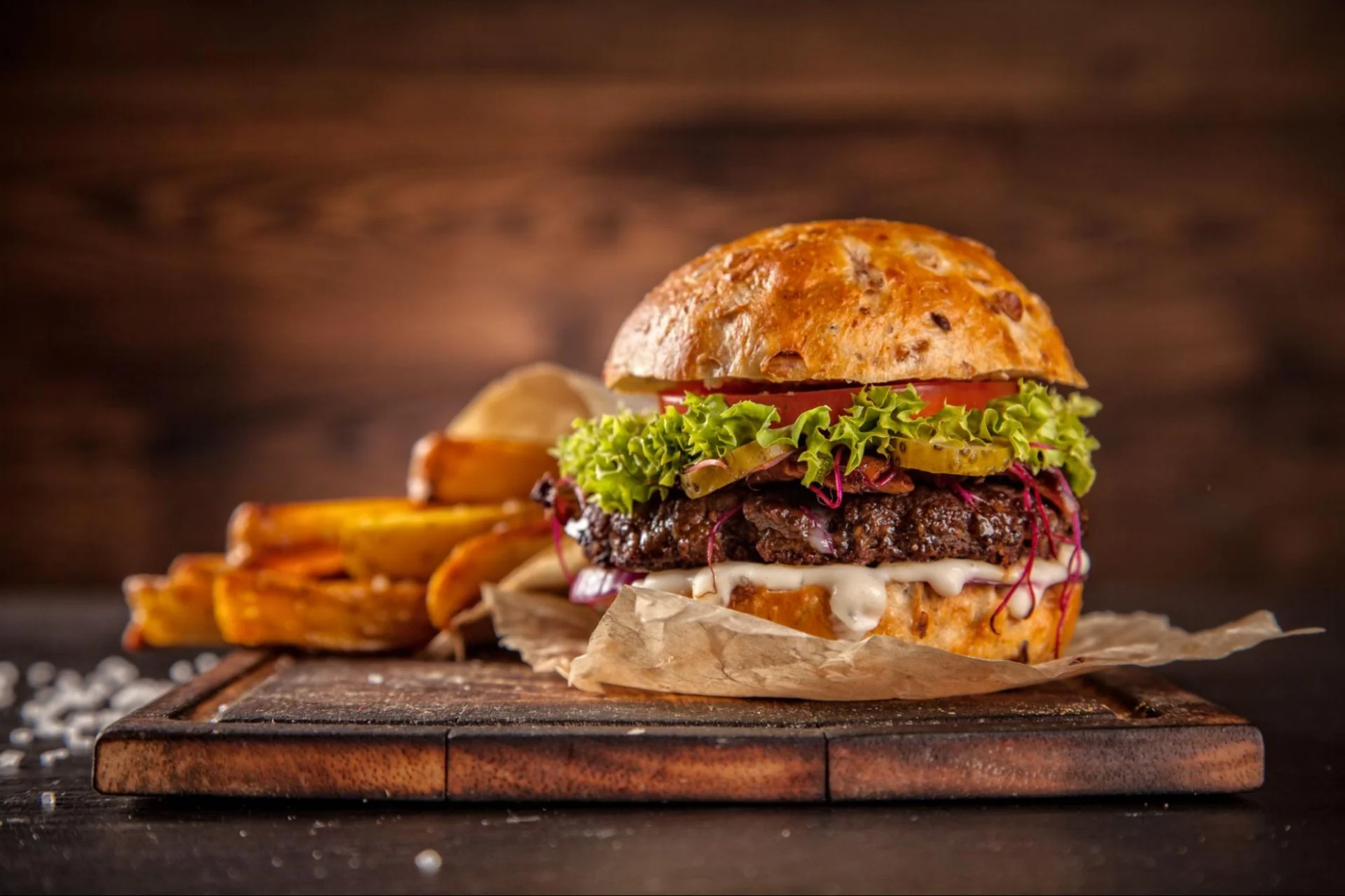 Burger with meat, vegetables, and fries served on a rustic surface