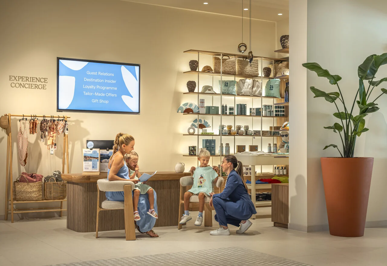 A mother with children speaking to an Experience Concierge staff member in a hotel area with offers for guests and families.