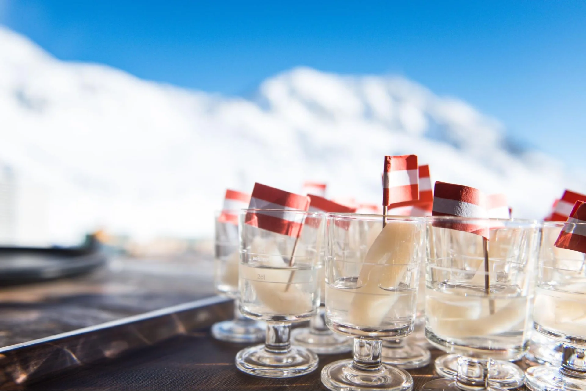 Several shot glasses printed with the red and white Austrian flag standing side by side on a table.