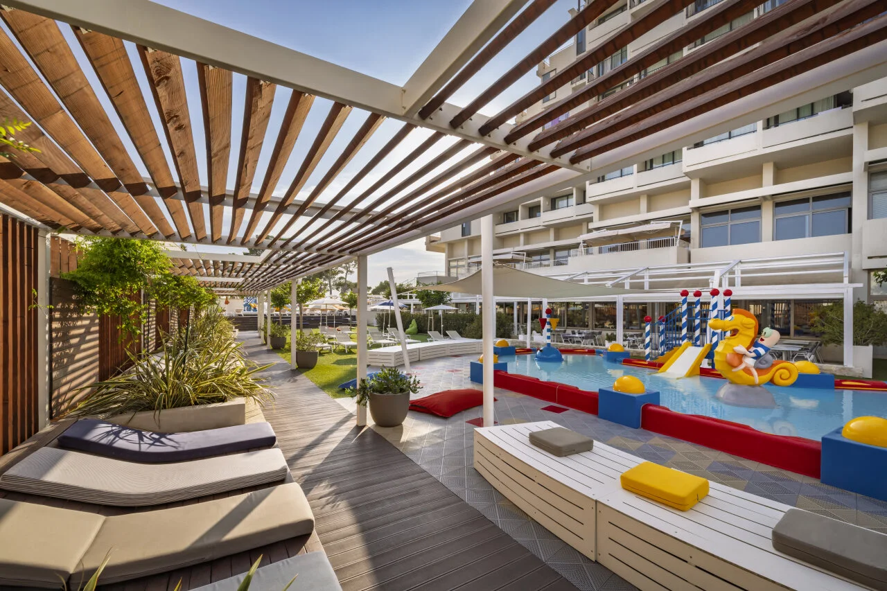An outdoor children’s pool with slides, sprinklers and a relaxation area in a family resort.