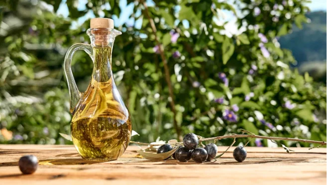 Bottle of olive oil and fresh olives on a wooden table in a garden setting